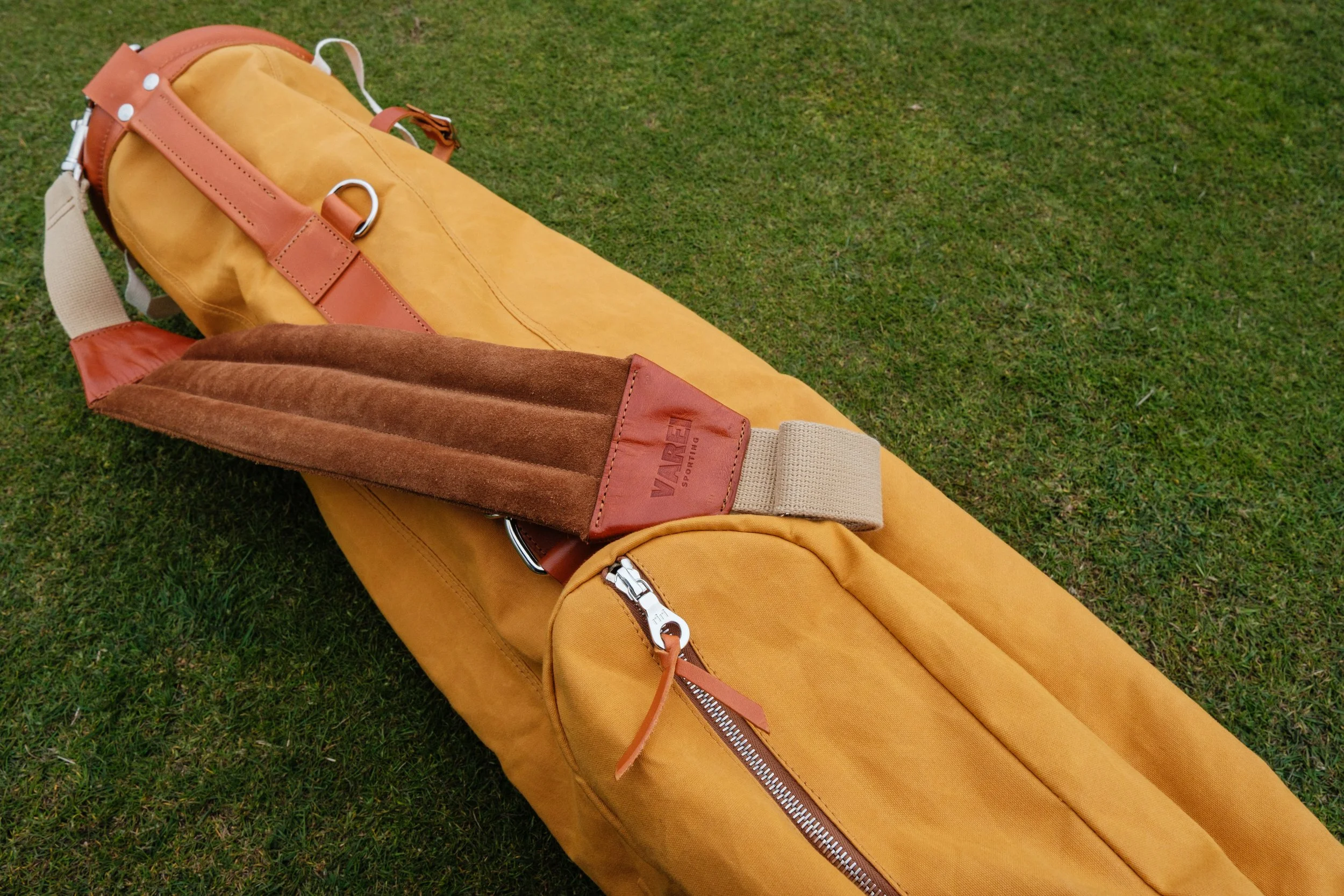 Yellow golf bag with a brown padded strap, lying on green grass.