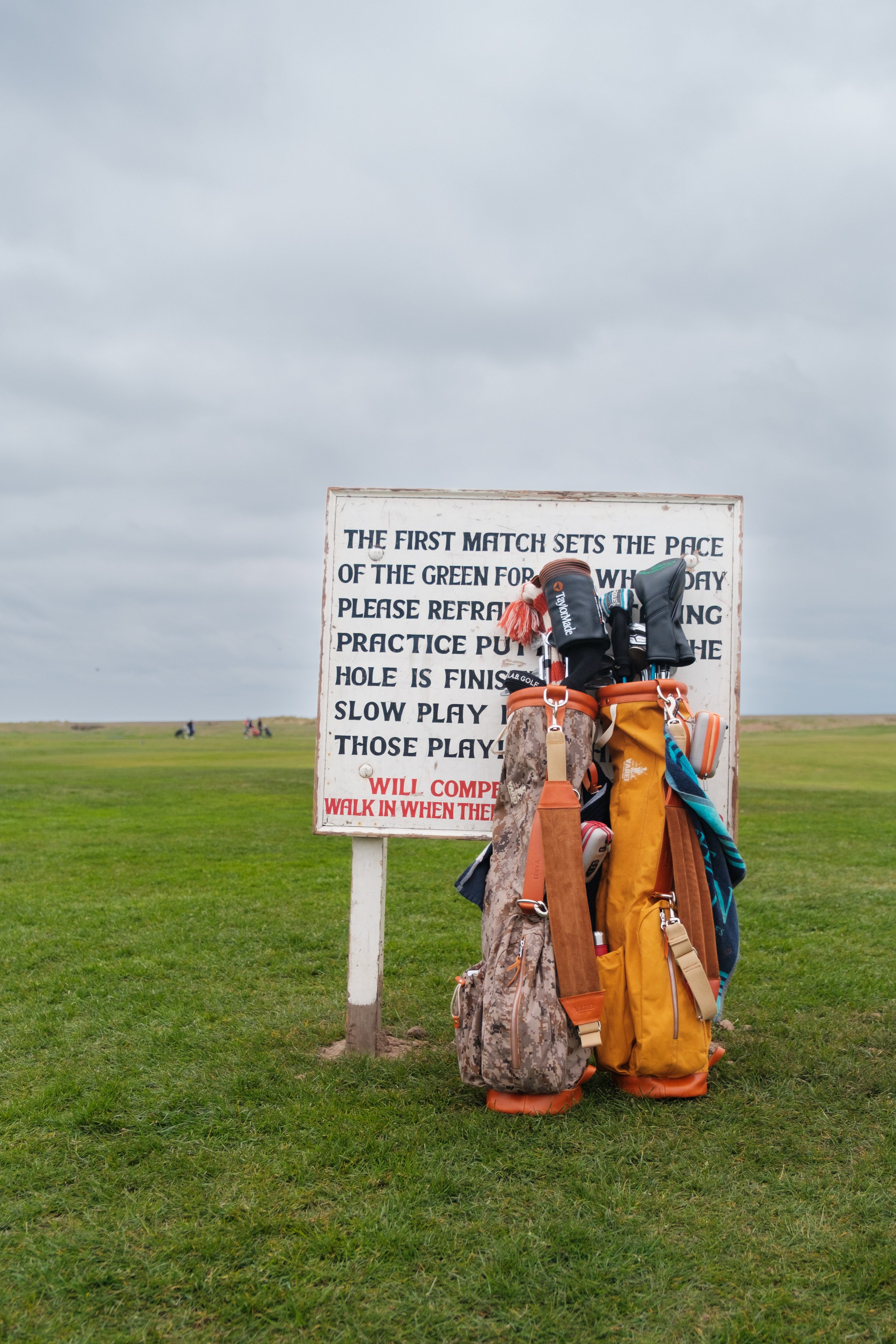 A golf course with a set of golf bags and clubs standing on grass near a sign with instructions for playing