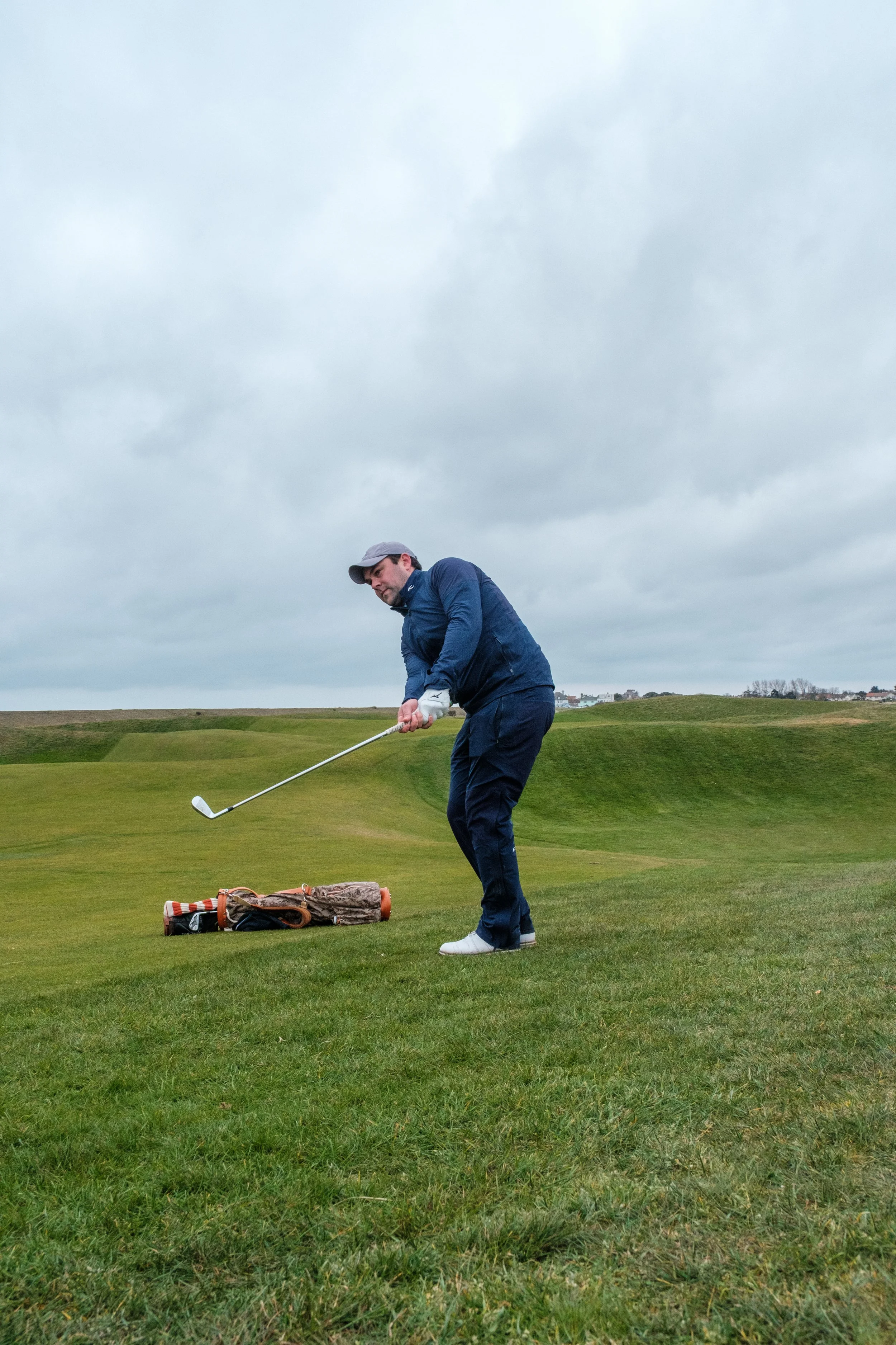 A man playing golf on a lush green golf course under a cloudy sky.