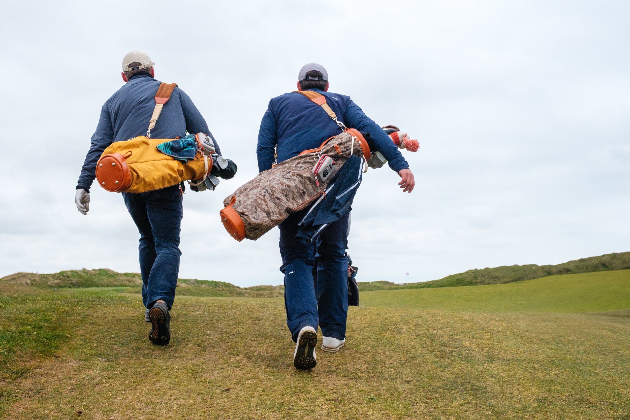 Two men walking on a golf course carrying golf bags with clubs.