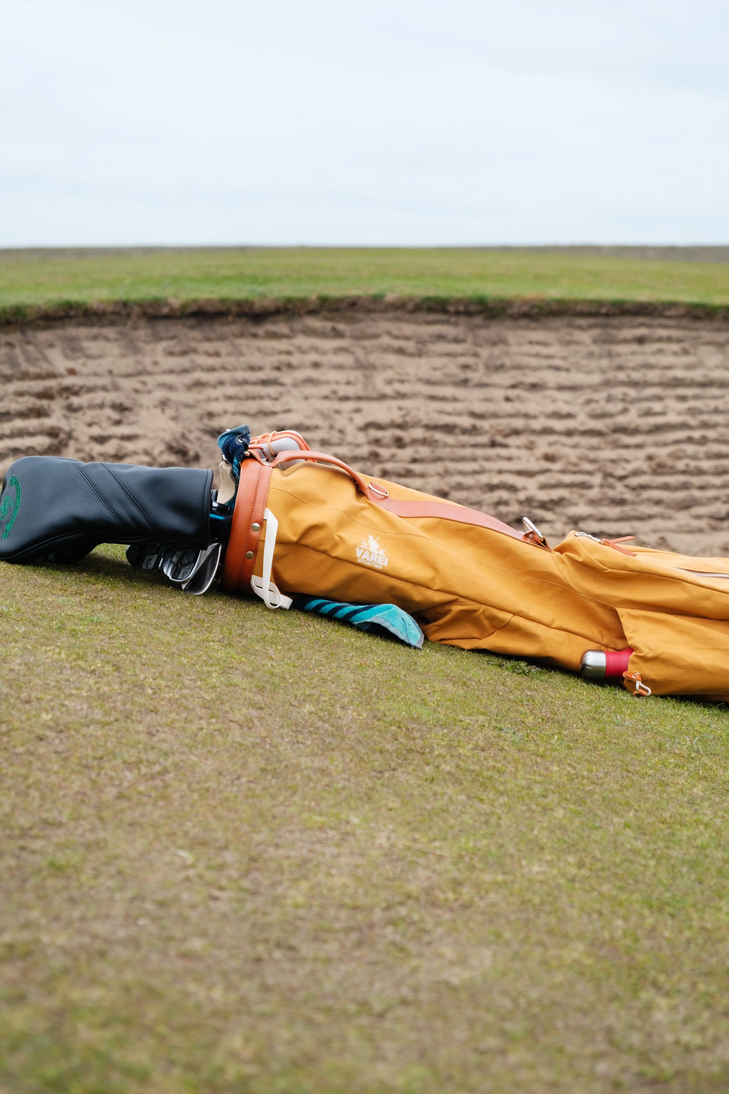 A golf course with a golf bag and clubs lying on the grass next to a sand trap.
