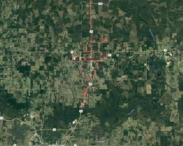 Satellite view of a small town surrounded by agricultural fields, with roads connecting it to the wider area.