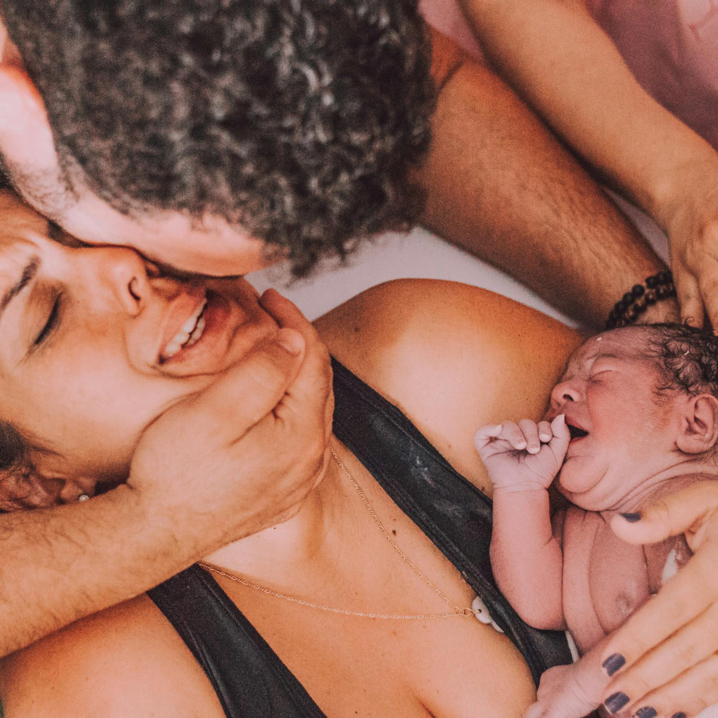 A mother holding a newborn baby with a man embracing her supportively.