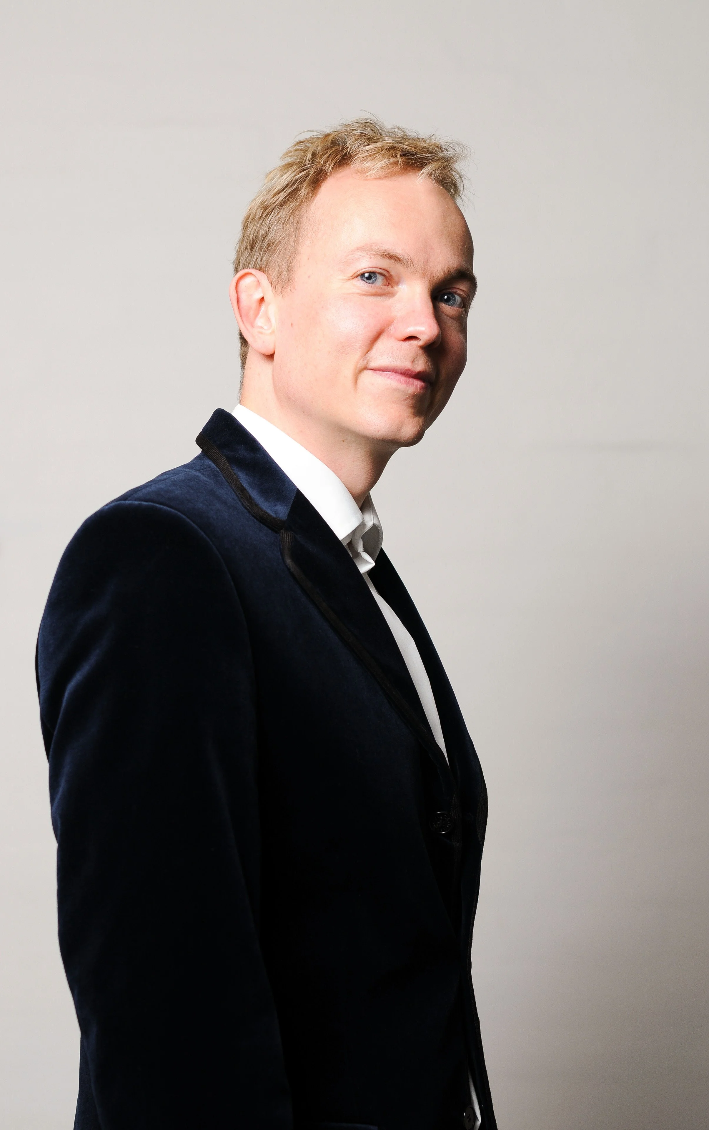 Et portrætbillede af en mand med blond, kort hår, iført blåt jakkesæt og hvid skjorte, der står mod en lys baggrund.