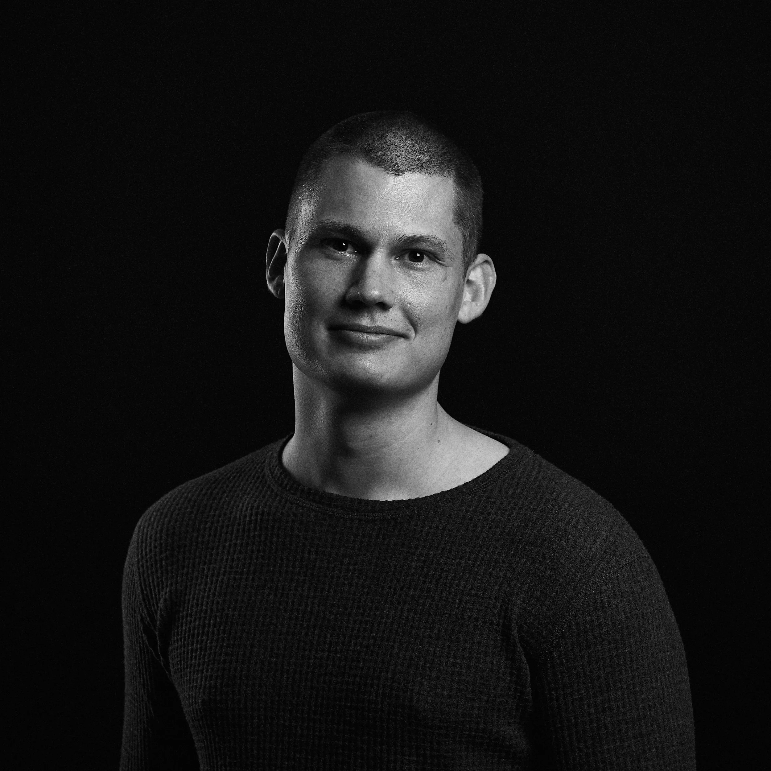 Sort-hvid portrætfotografi af en ung mand med kort hår, iført sort sweater, med neutral baggrund.