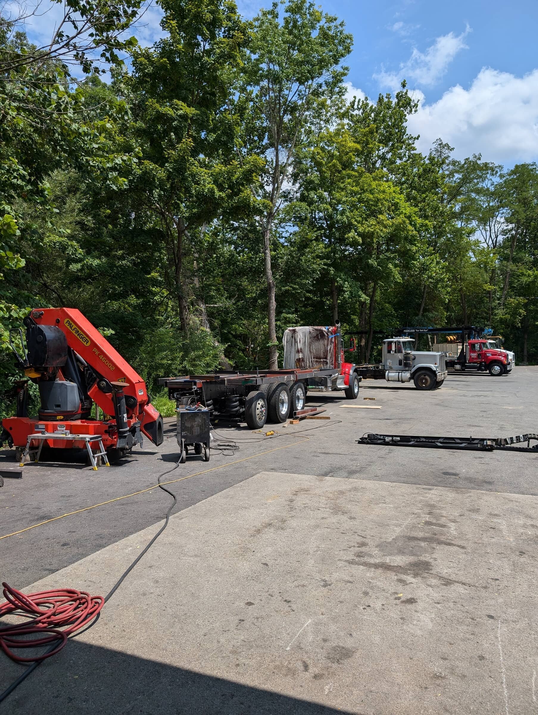 Construction site with trucks and equipment, surrounded by trees and a partly cloudy sky.