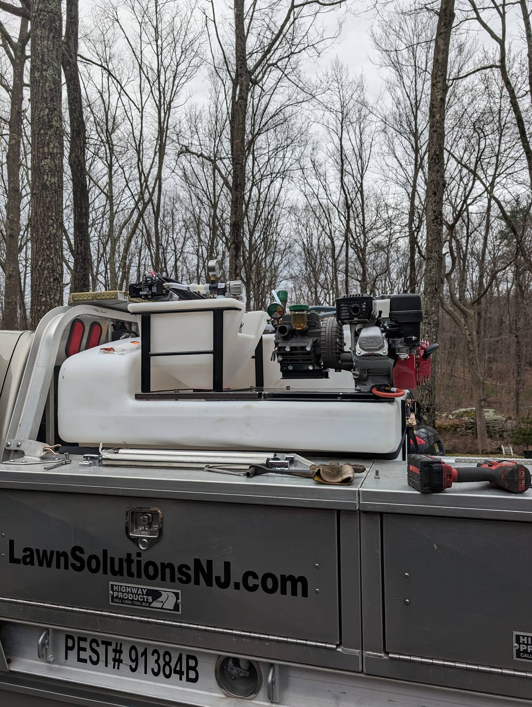 Lawn care equipment and tools on a trailer with a background of leafless trees.