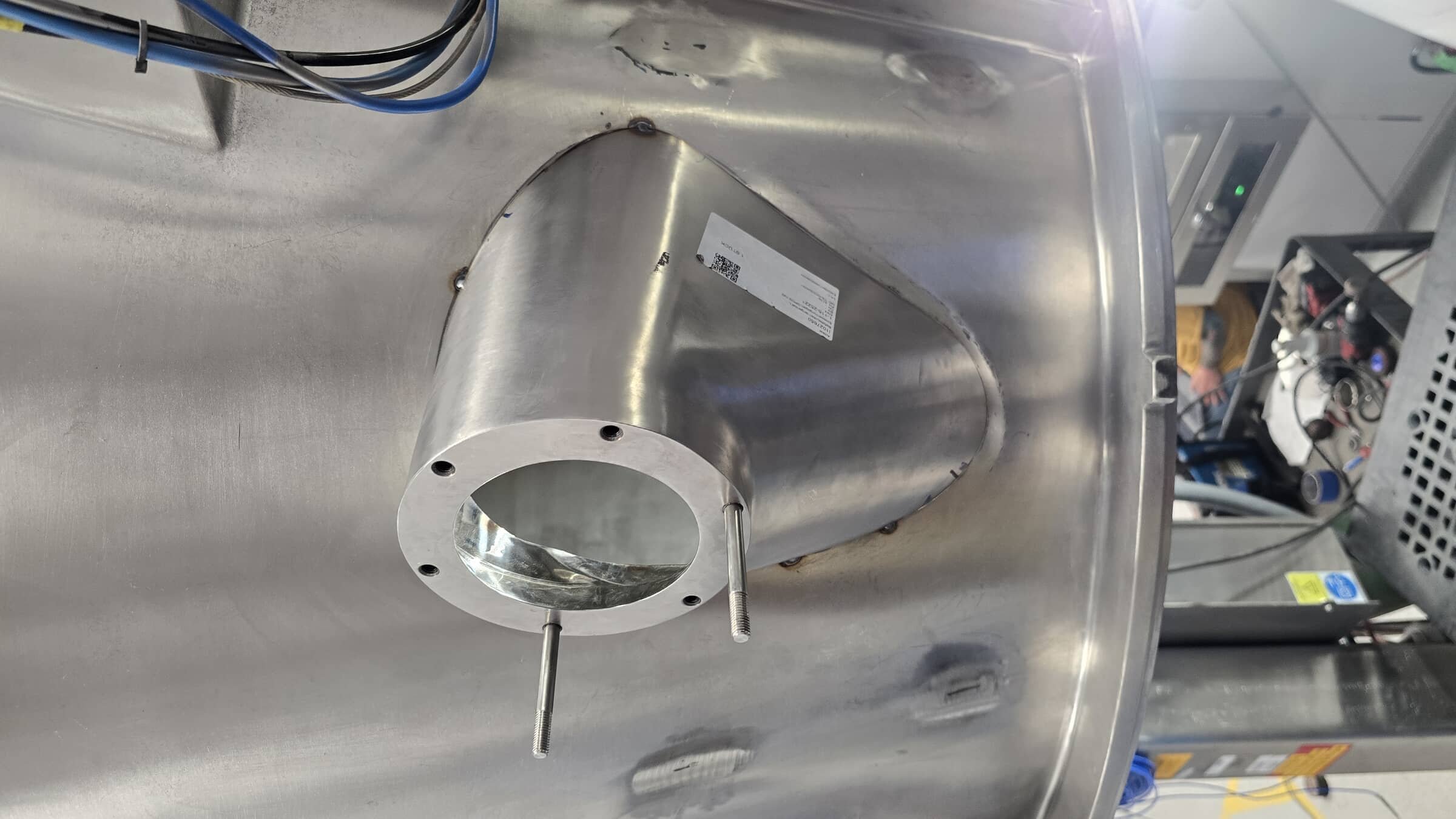 A metallic mechanical component with a large circular opening and a conical shape mounted on a metal workbench in an industrial setting.