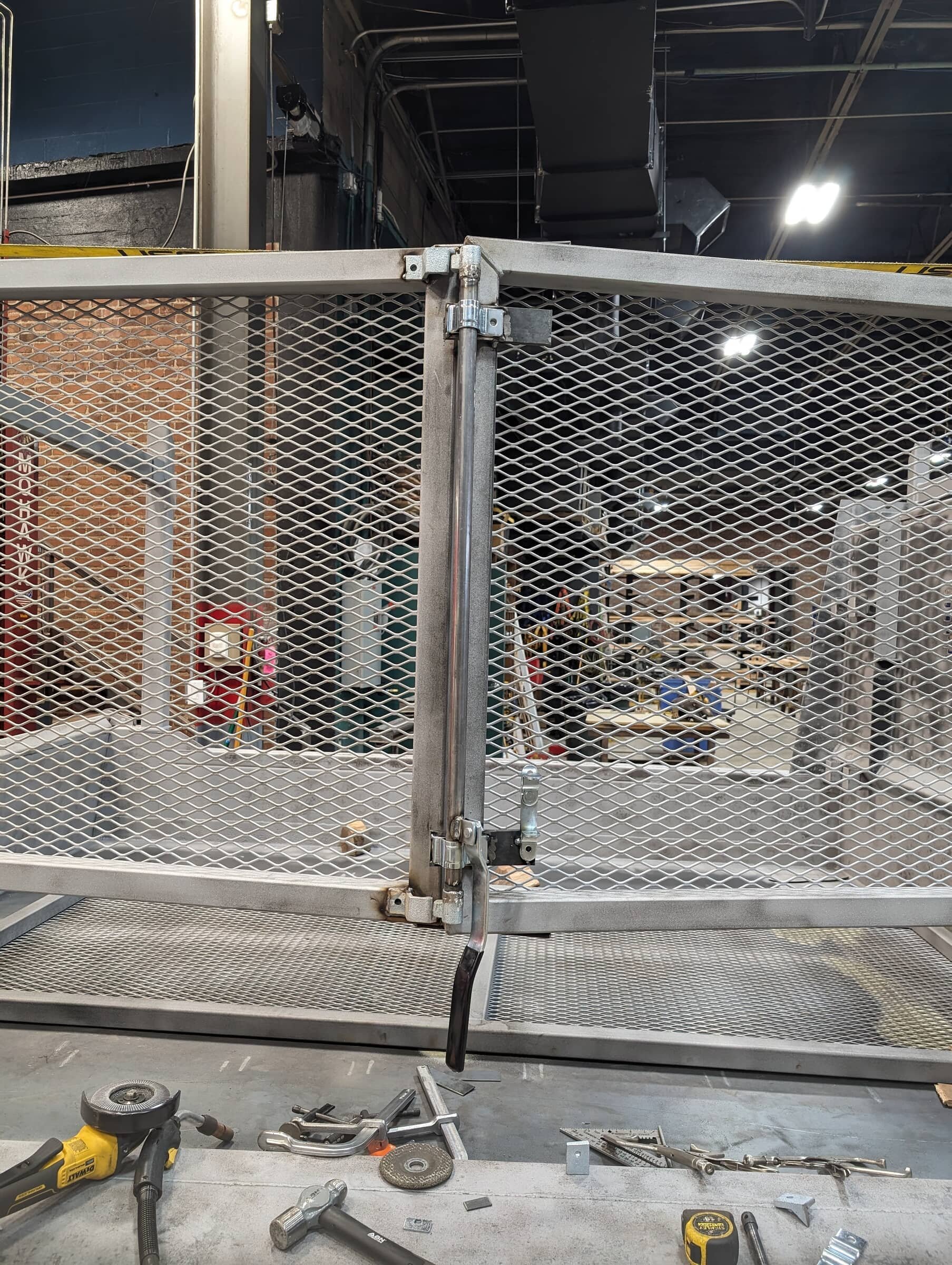 A metal workshop workspace with a partially assembled metal gate, tools such as a angle grinder, hammer, measuring tape, and screws on the workbench.