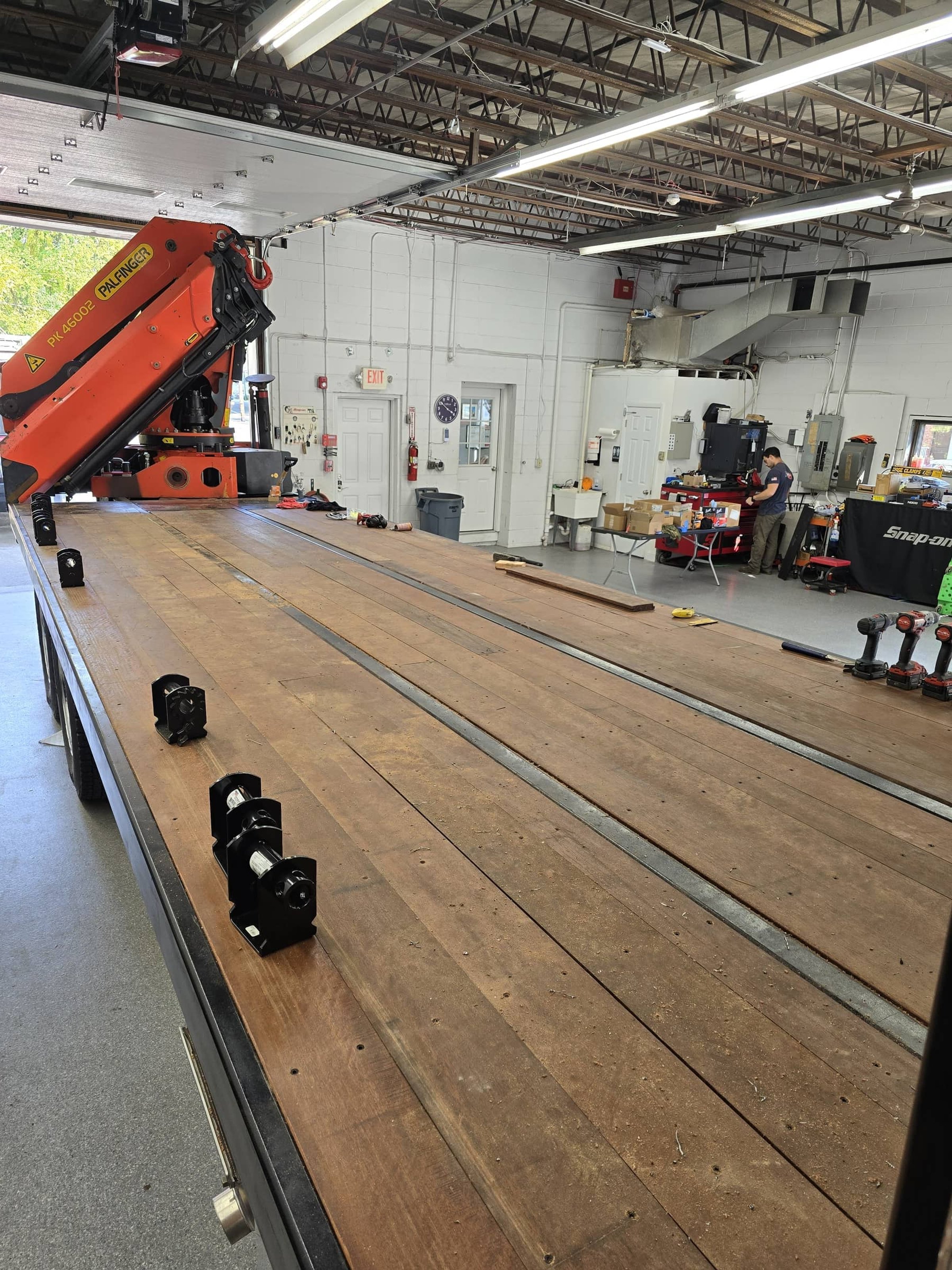 A workshop with a large wooden workbench, tools, and equipment, including an orange robotic arm, with a person working in the background.