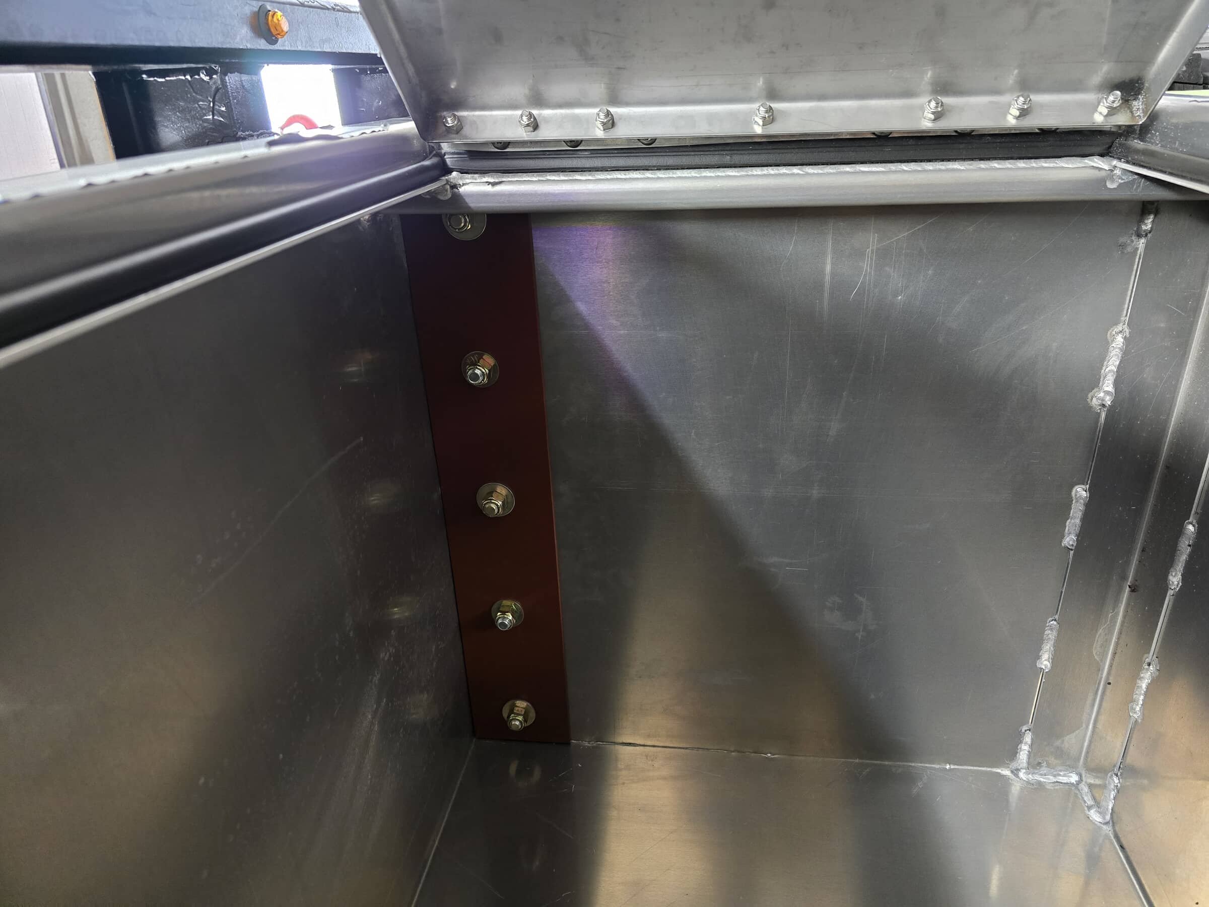 The interior of a metal box or machine with visible screws and welding points, showing the inside walls and part of the lid.