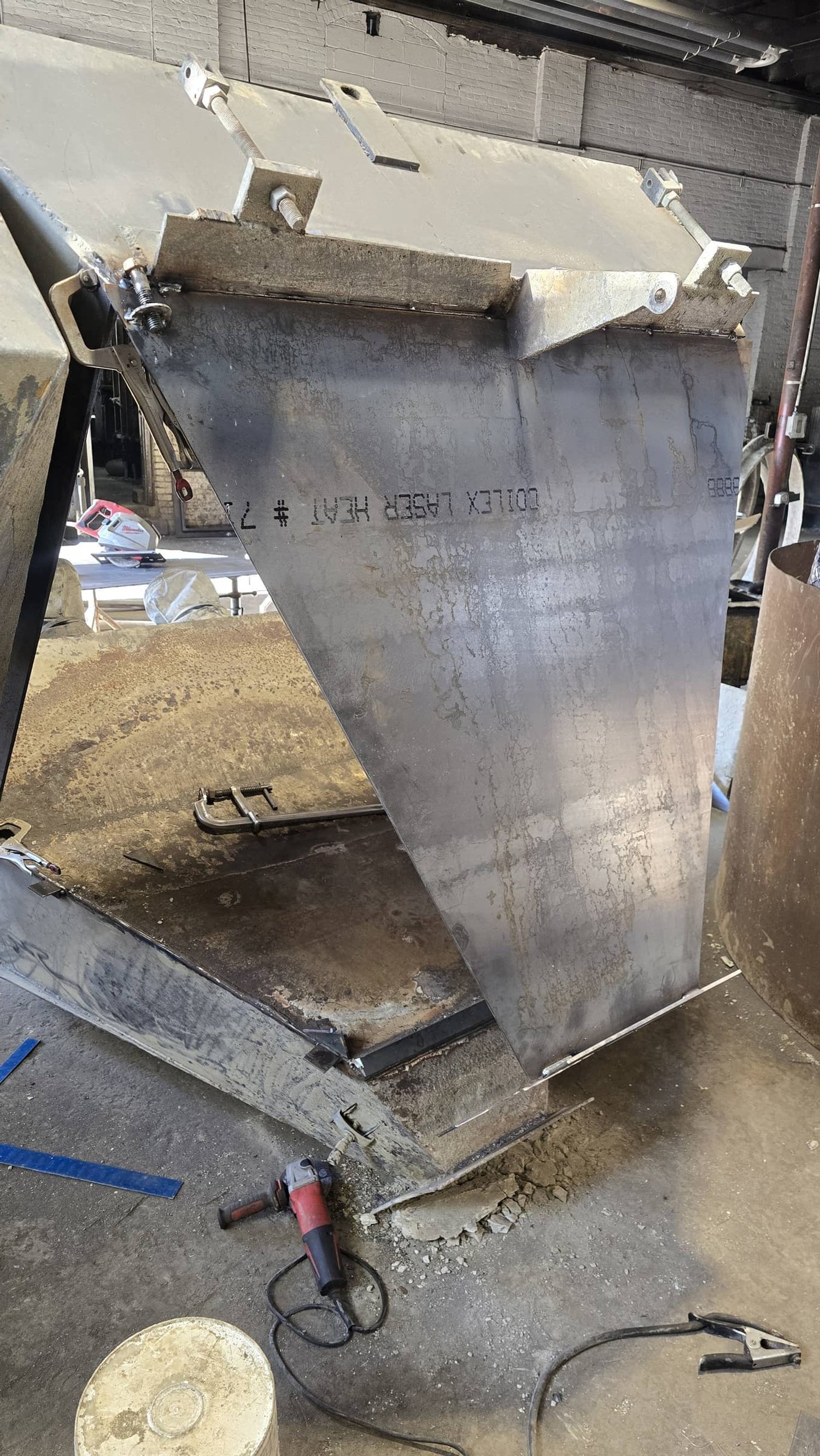A large metal fabrication or industrial equipment part being assembled or welded, with tools and clamps nearby, in a workshop setting.