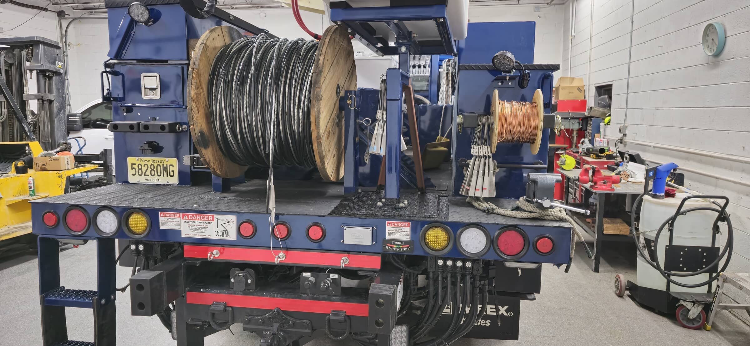 The back of a utility truck with large spools of wire, surrounded by tools and equipment in a workshop.