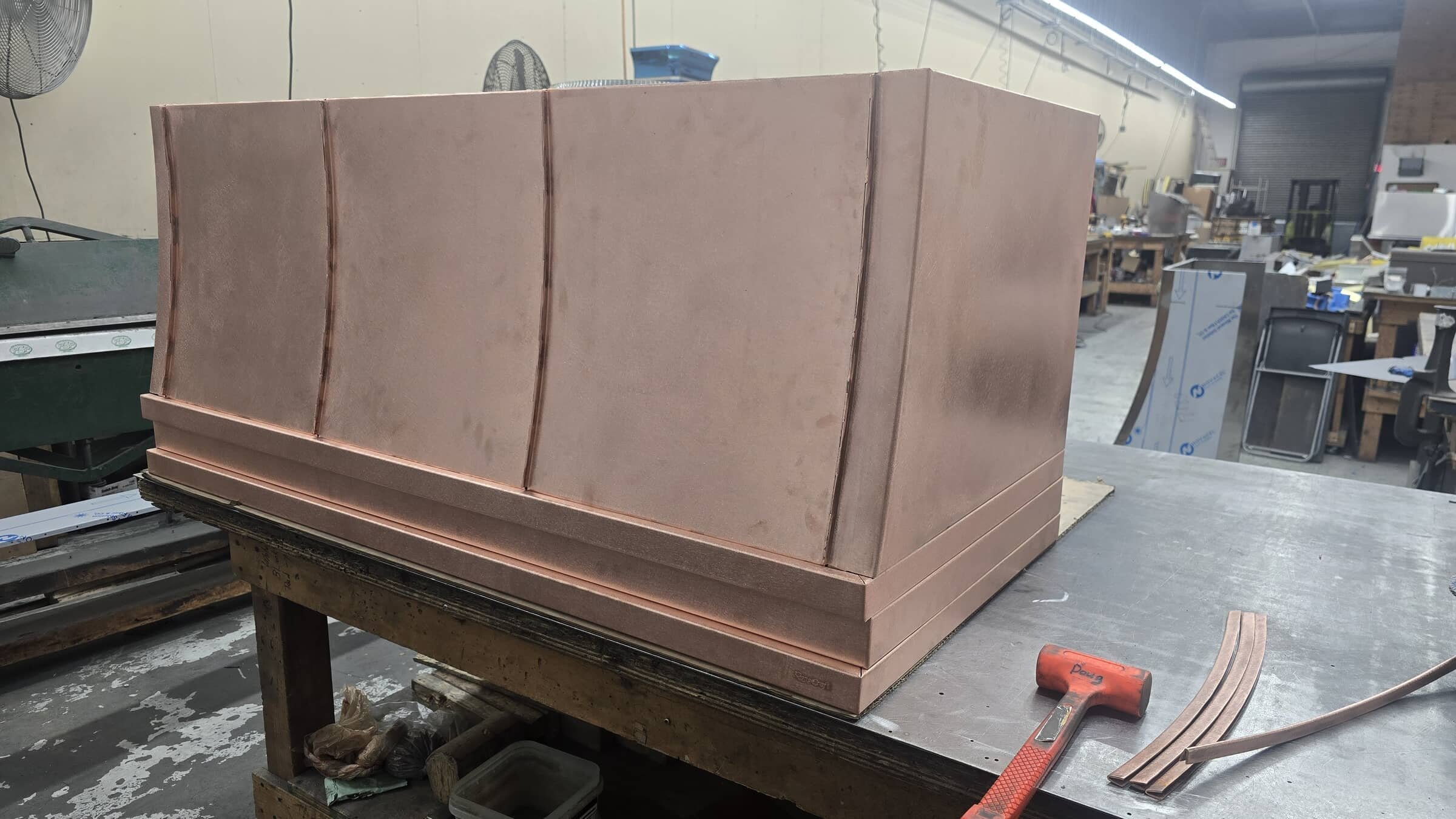 A copper mold with a stepped design on a workbench in a workshop, with tools and equipment in the background.