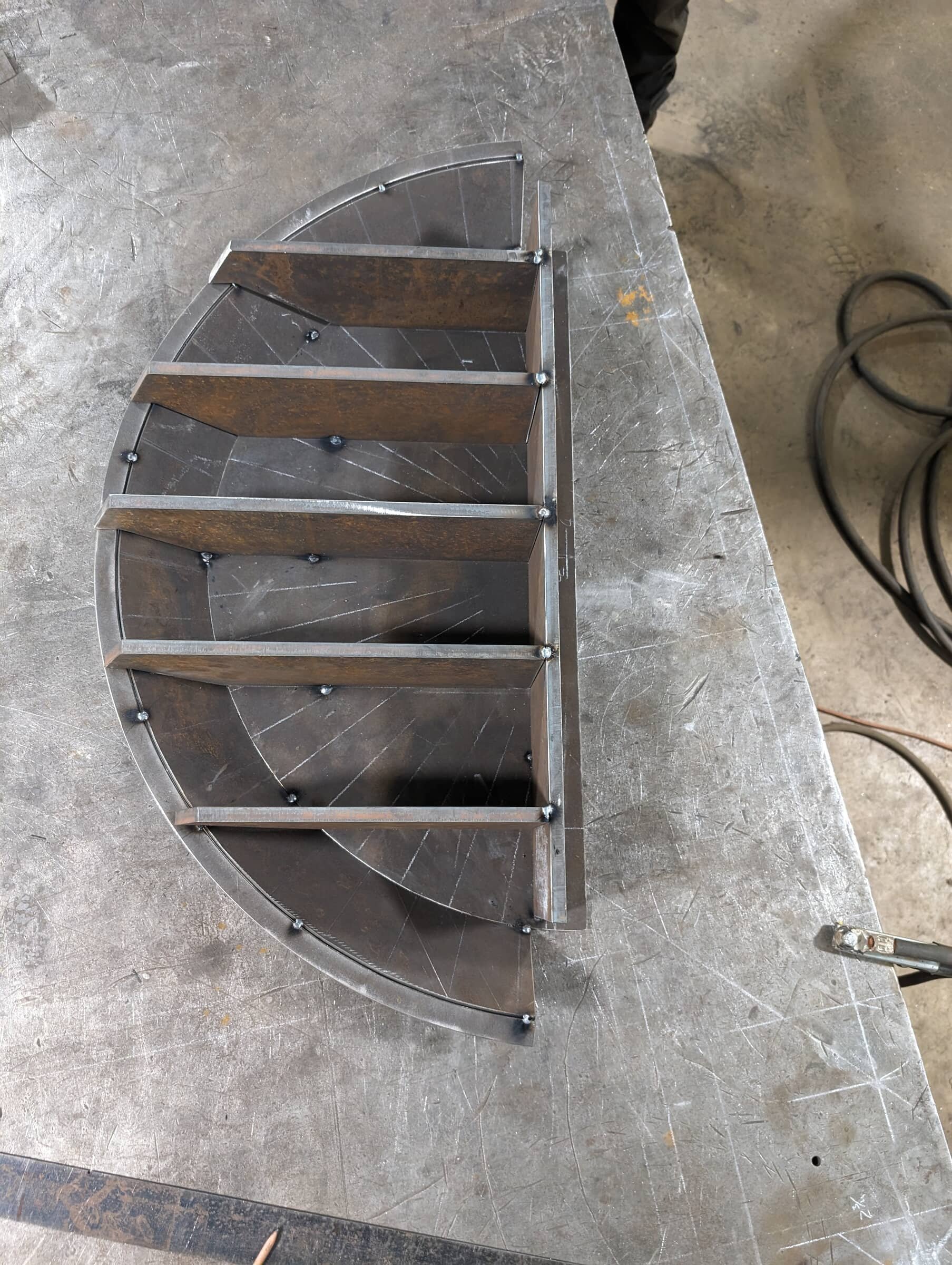A semi-circular metal structure with internal supports on a worktable in a workshop.