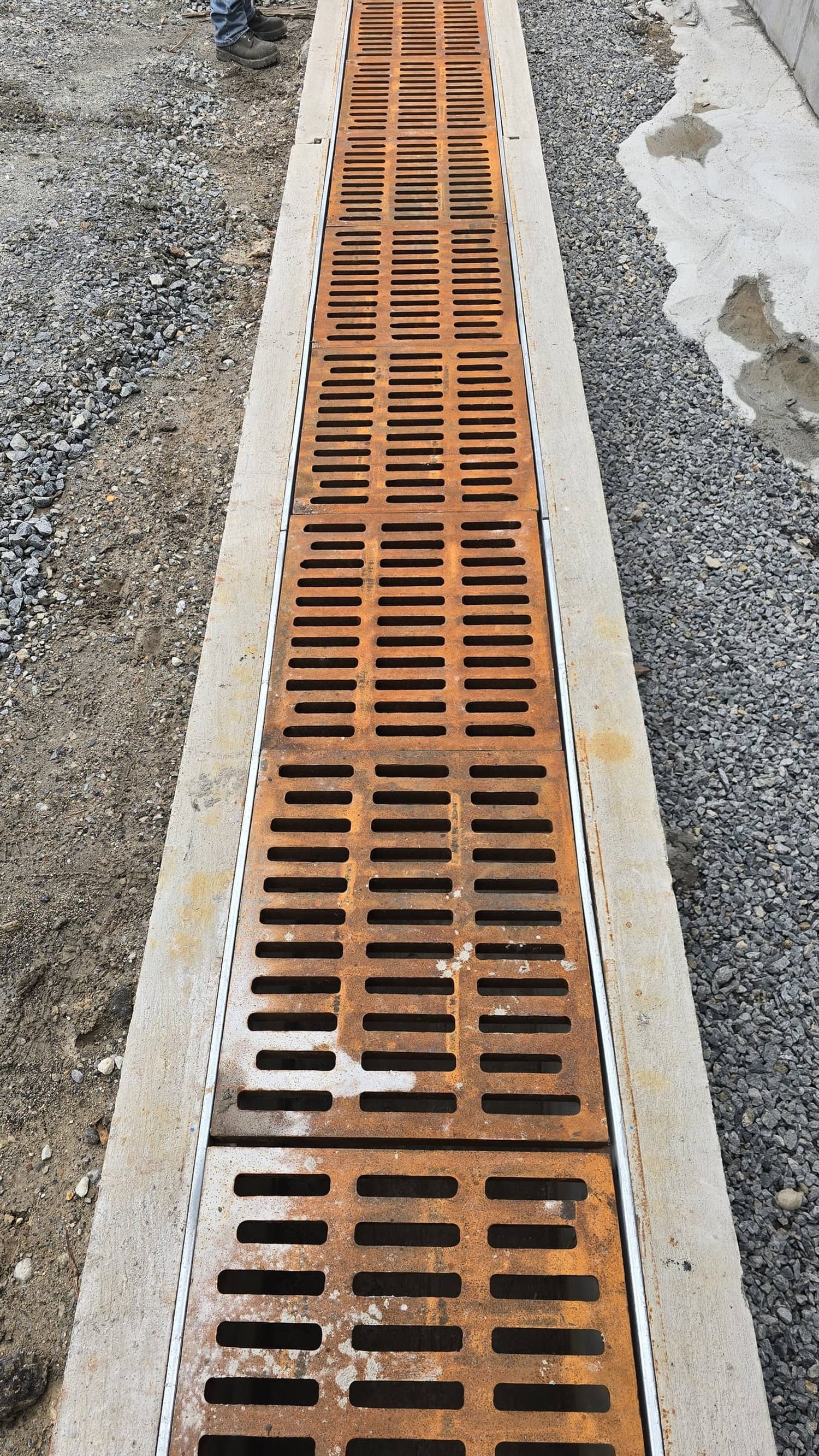 Metal drainage grate on concrete curb at a construction site.