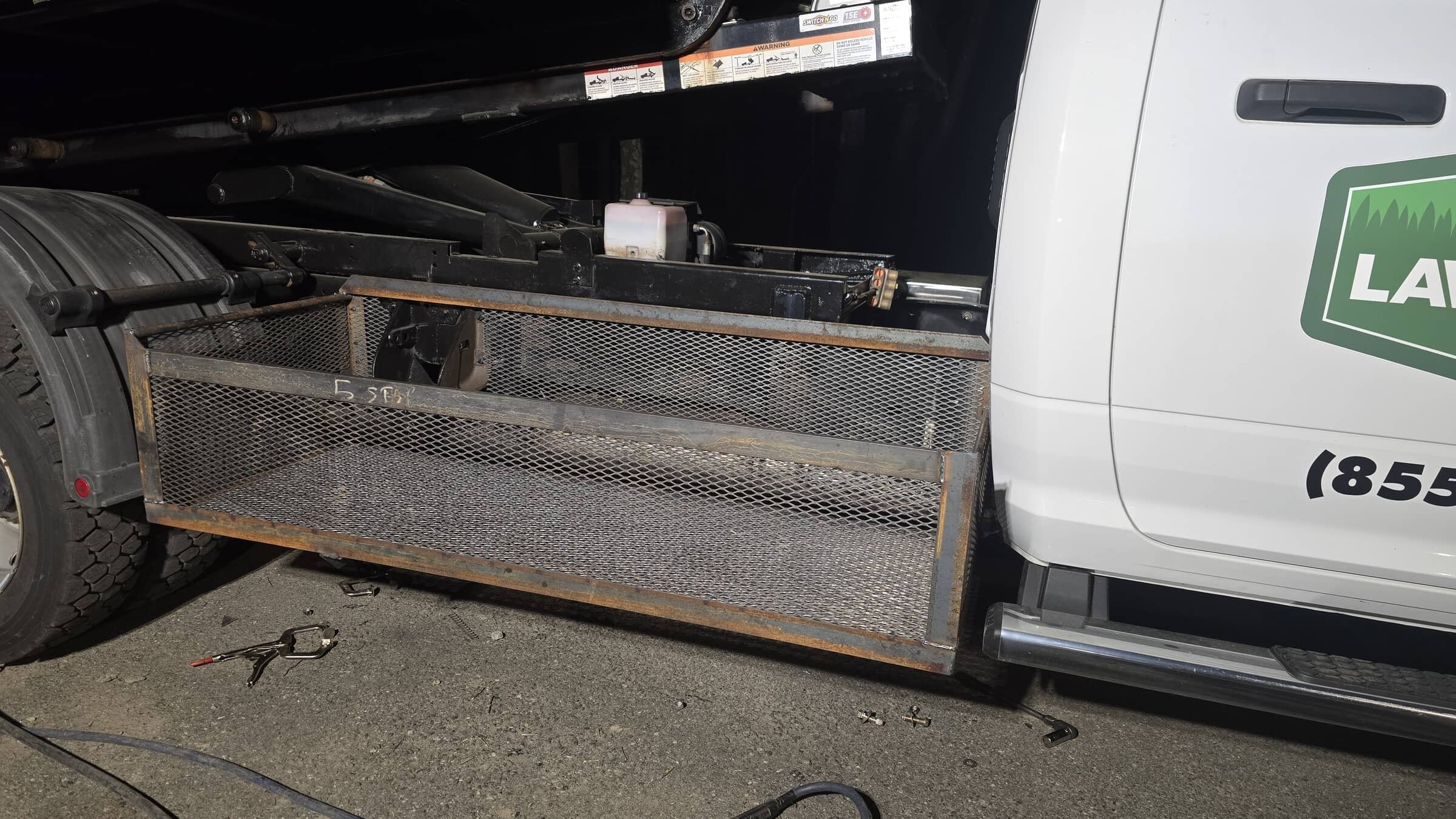 Close-up of a utility truck with metal storage compartments and hook tools on the ground.