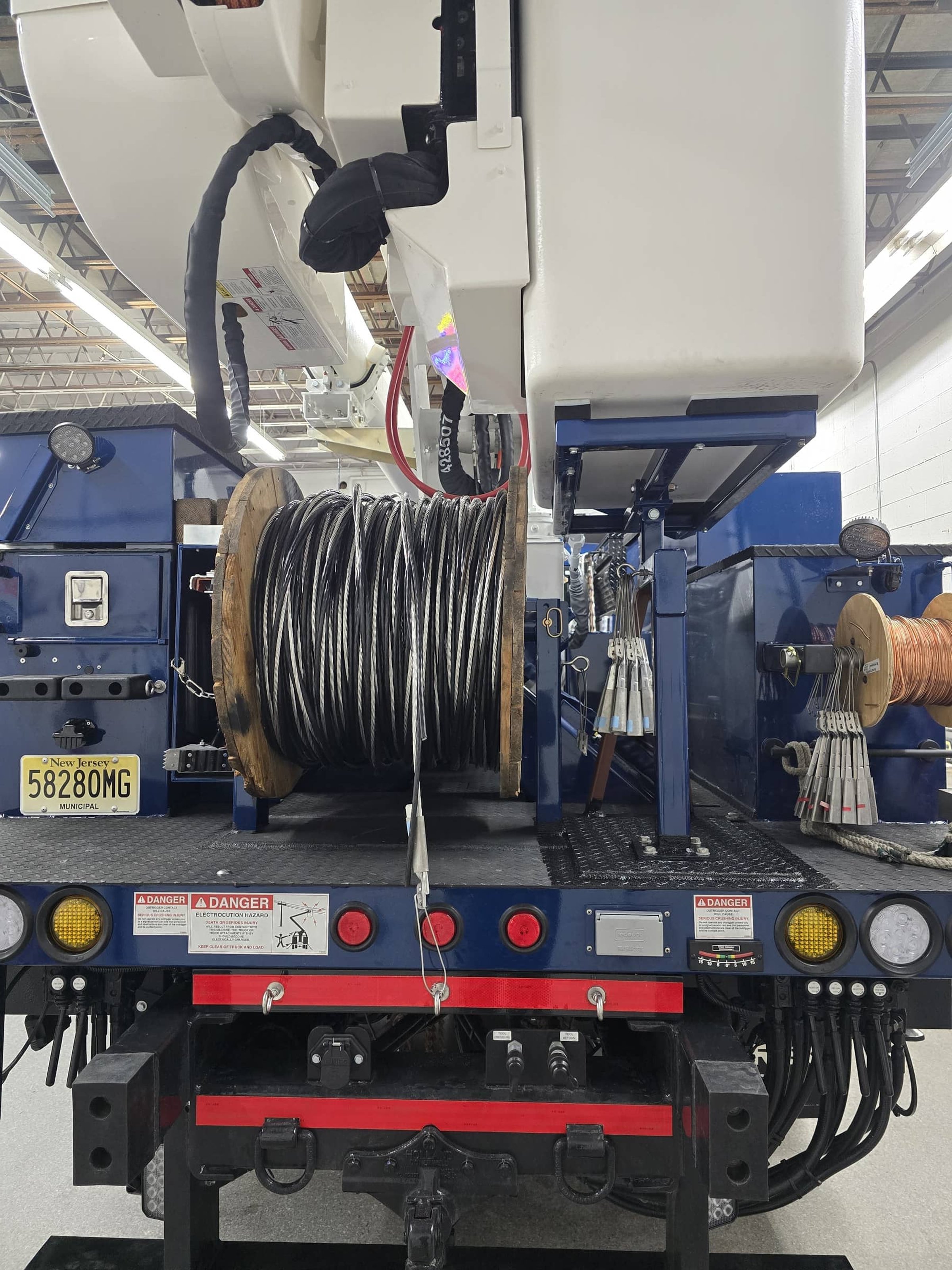Back of a utility truck with coiled cables, warning labels, and various electrical equipment.