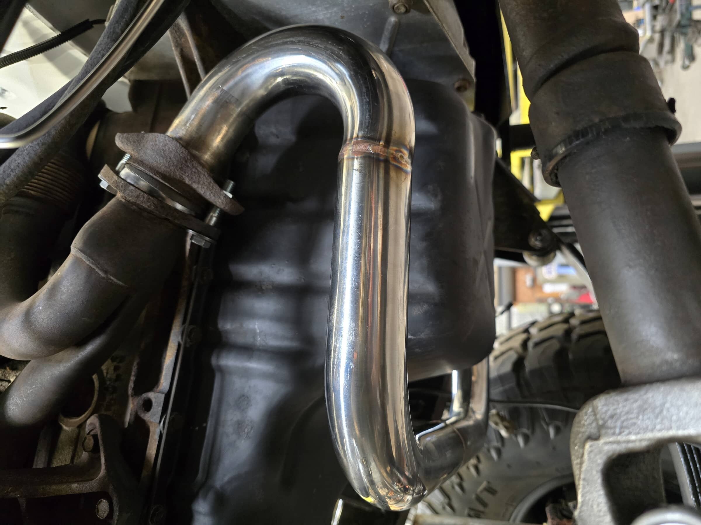 Close-up view of a shiny, new metal pipe installed in an engine bay, surrounded by black hoses and components.