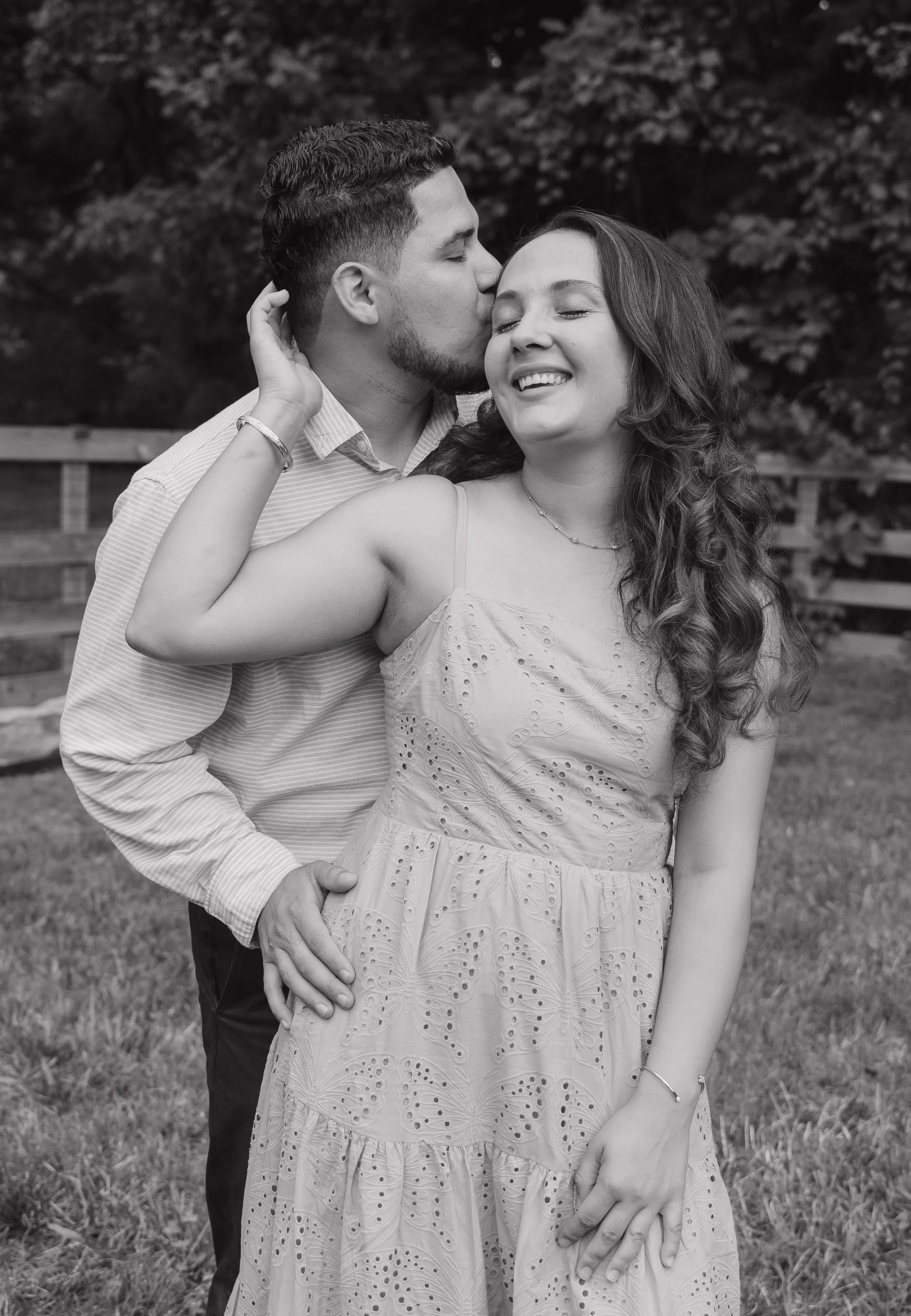 A couple shares an intimate moment, about to touch noses, outdoors with greenery in the background.