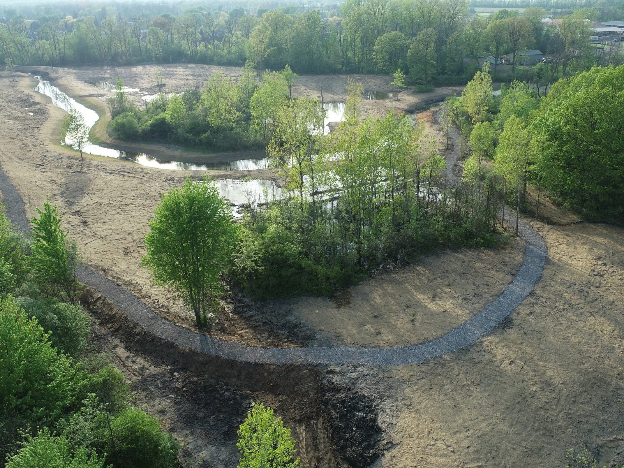 Aerial view of a natural landscape with a winding path through green trees and a body of water.