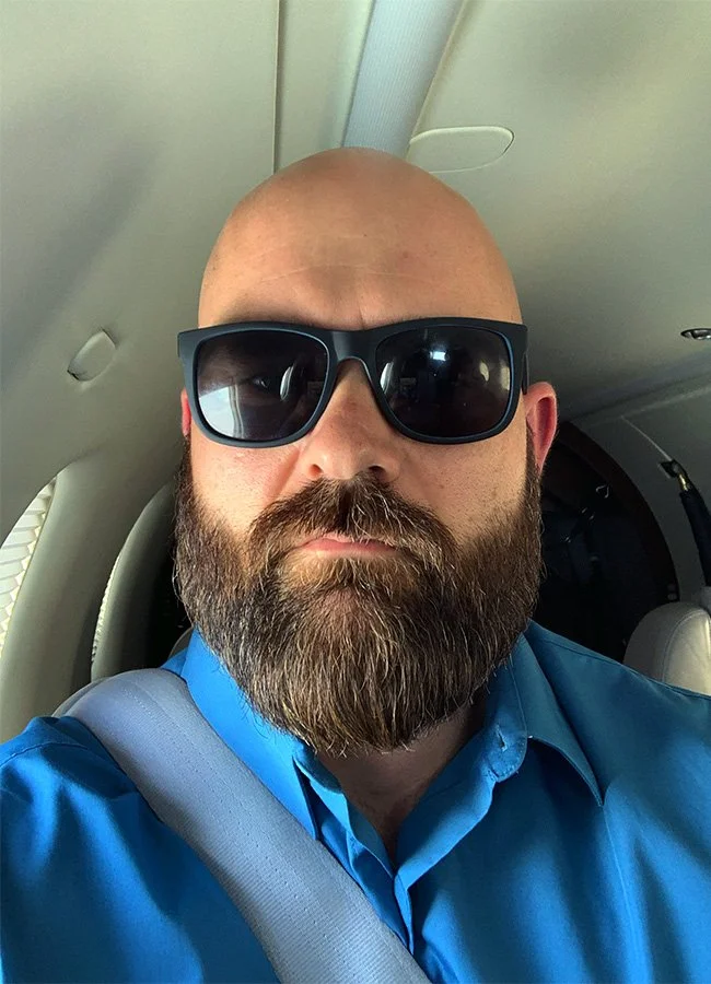 Mike Hirschfield confidently wearing dark sunglasses and a blue shirt inside a private jet.