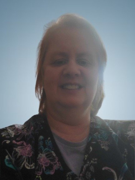 A woman smiling wearing a patterned top with a bright blue sky in the background.