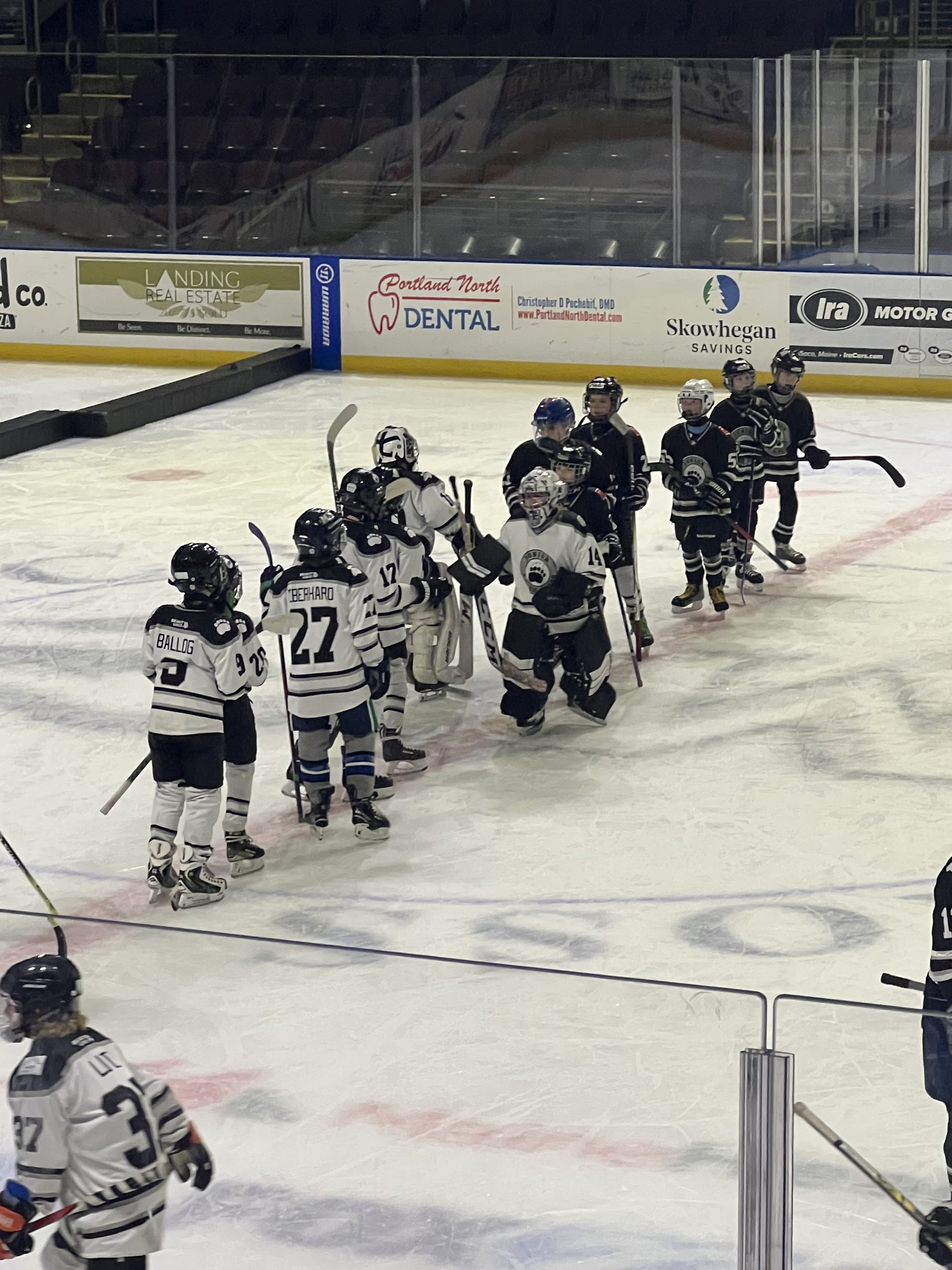 Hockey players in black and white uniforms shaking hands on the ice after a game, with empty stands and advertisements in the background.