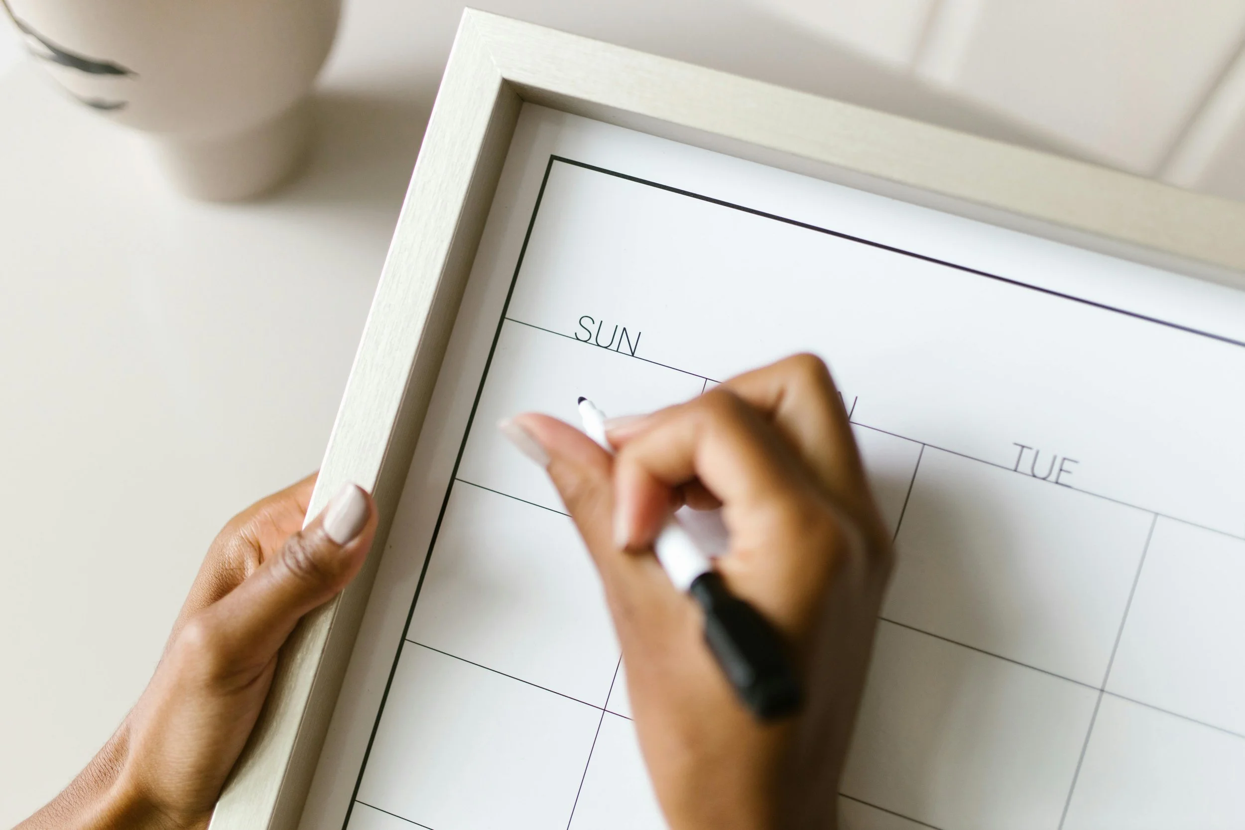 woman's hand writing on a weekly wipe-off calendar with a pen