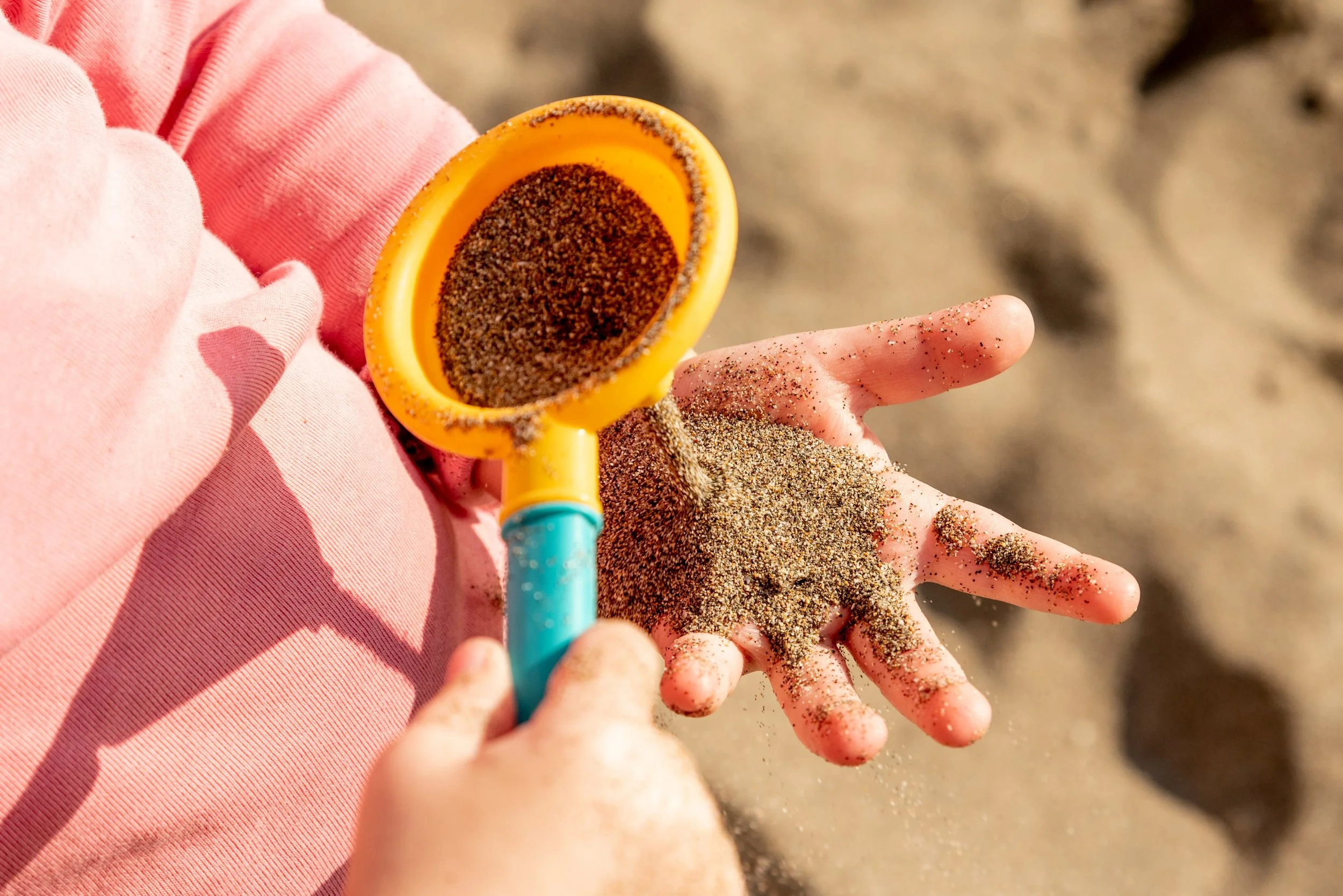 Child playing with sand using a yellow shovel on the beach