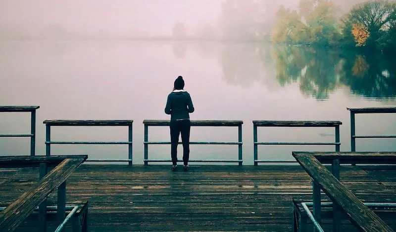 A woman standing by a lake in the fog