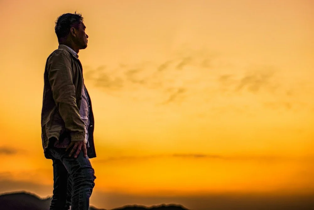 A man looking away with the sunset behind him