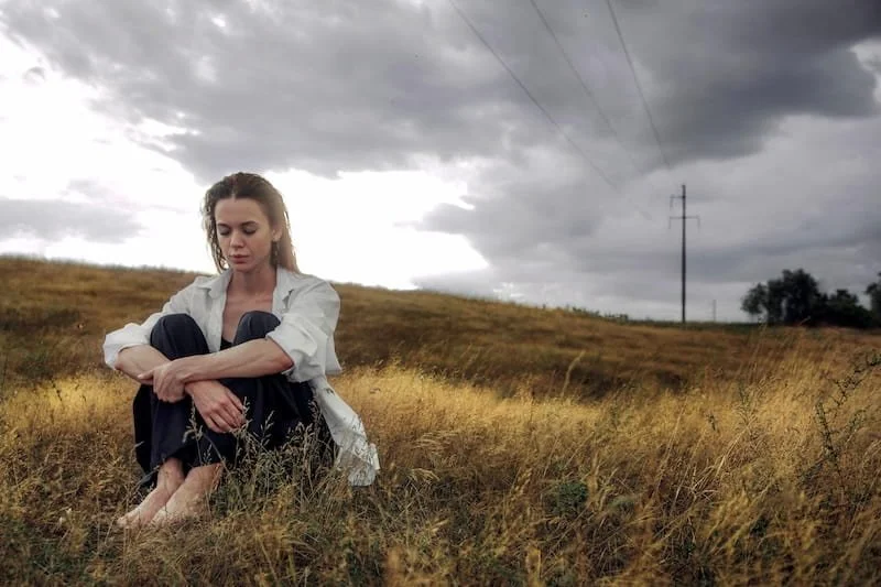 A woman sitting in a field barefoot