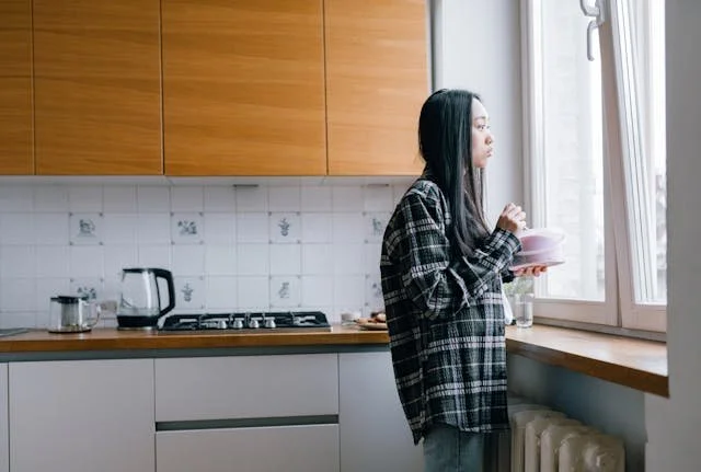 A woman looking out the window of her kitchen