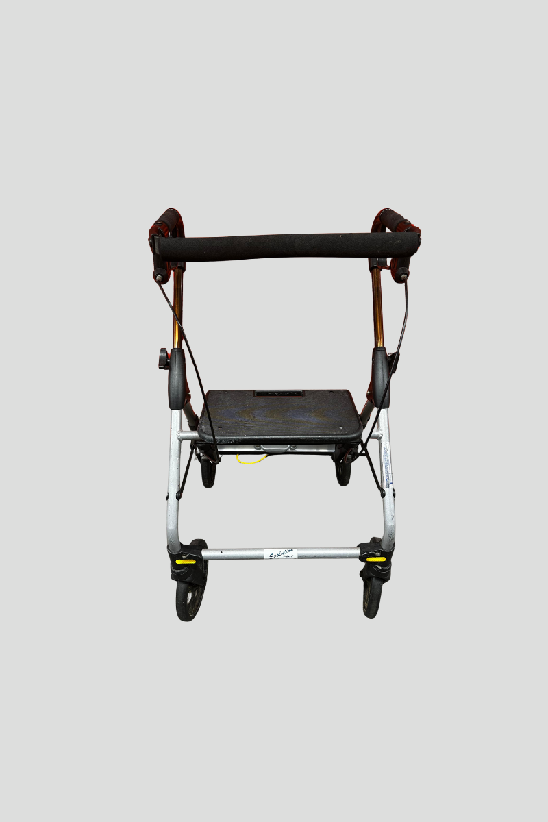 A four-wheeled walker with a black seat and padded handlebar rests in front of a red metal roll-up door on a multicolored carpeted floor.