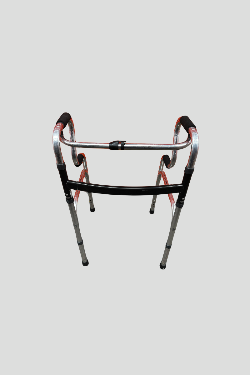 Silver walker with black handle grips in front of a red shutter door on a speckled carpeted floor.