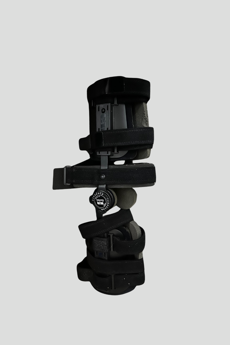 A black ski binding with adjustable components lying on a multicolored carpet.