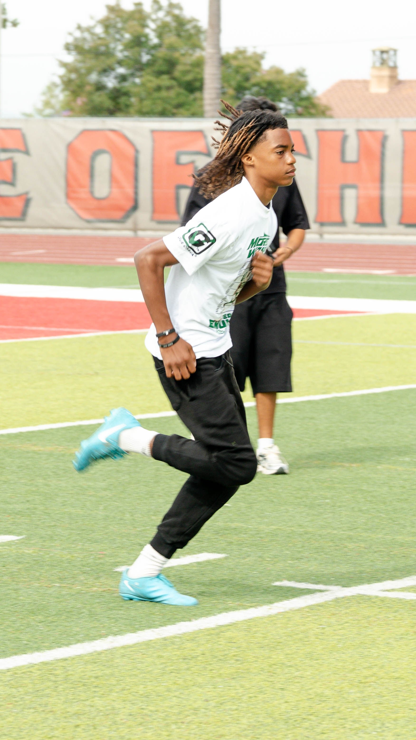 Young male athlete running on a track field during practice or a game, wearing athletic shoes and casual sportswear.