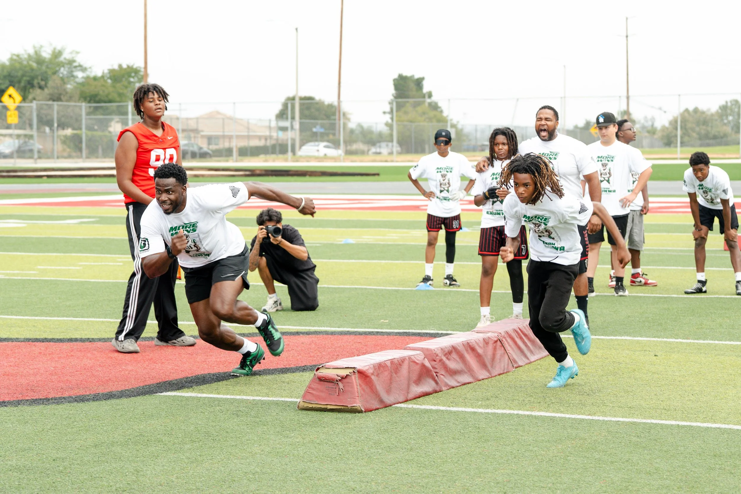 A group of children and an adult participating in a relay race event on a sports field, with some running and others waiting for their turn.