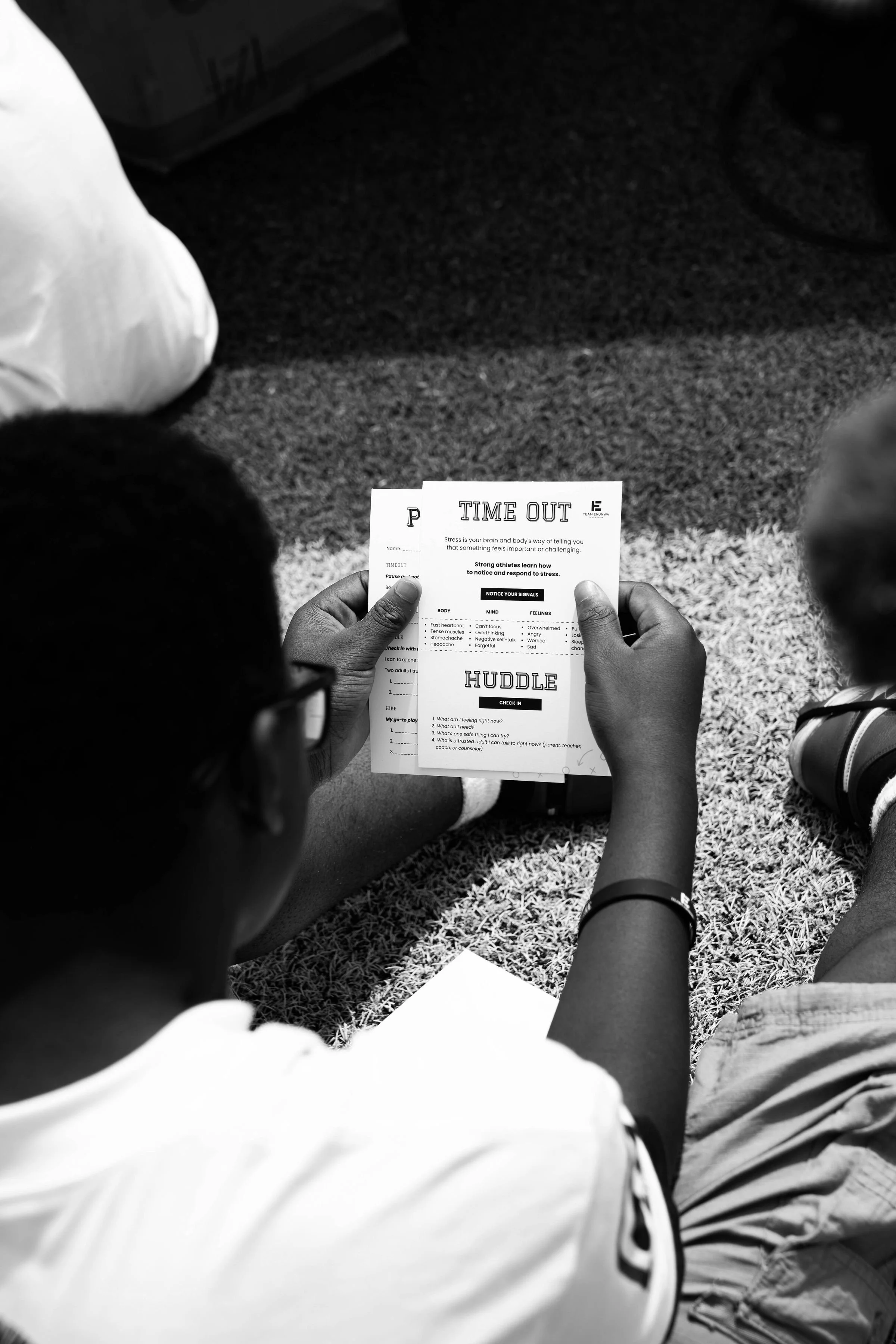 Someone holding a paper titled 'TIME OUT' with stress management information, sitting on grass outdoors with others.