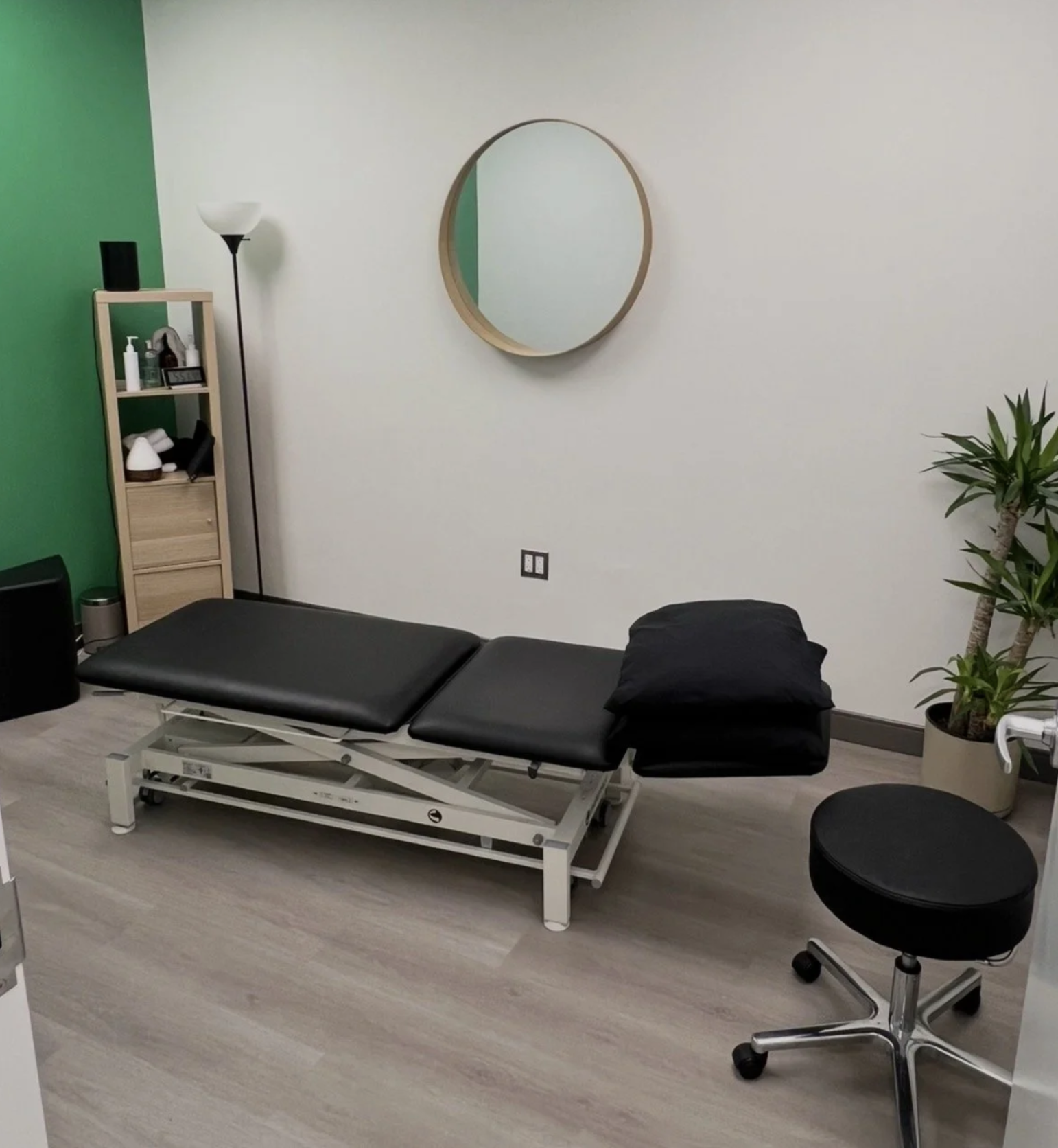 Treatment room with green accent wall, treatment table and stool