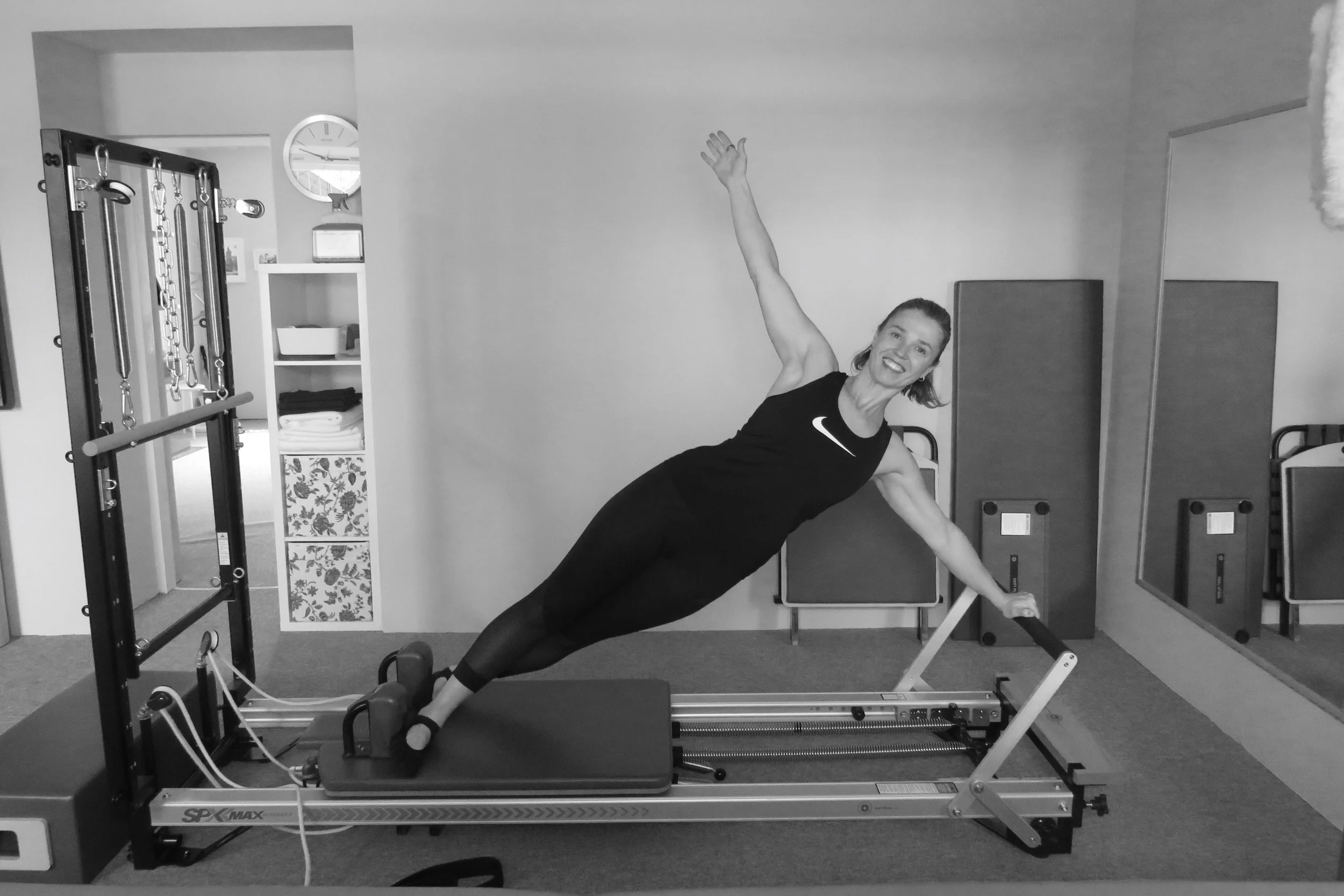 Woman in athletic attire performing a Pilates move on a reformer machine in a fitness studio.