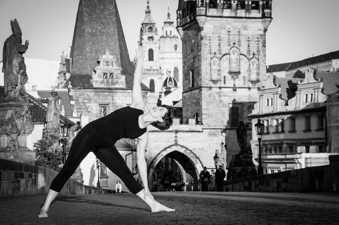 Woman practicing yoga outdoors near historic castle with towers and statues in Prague.