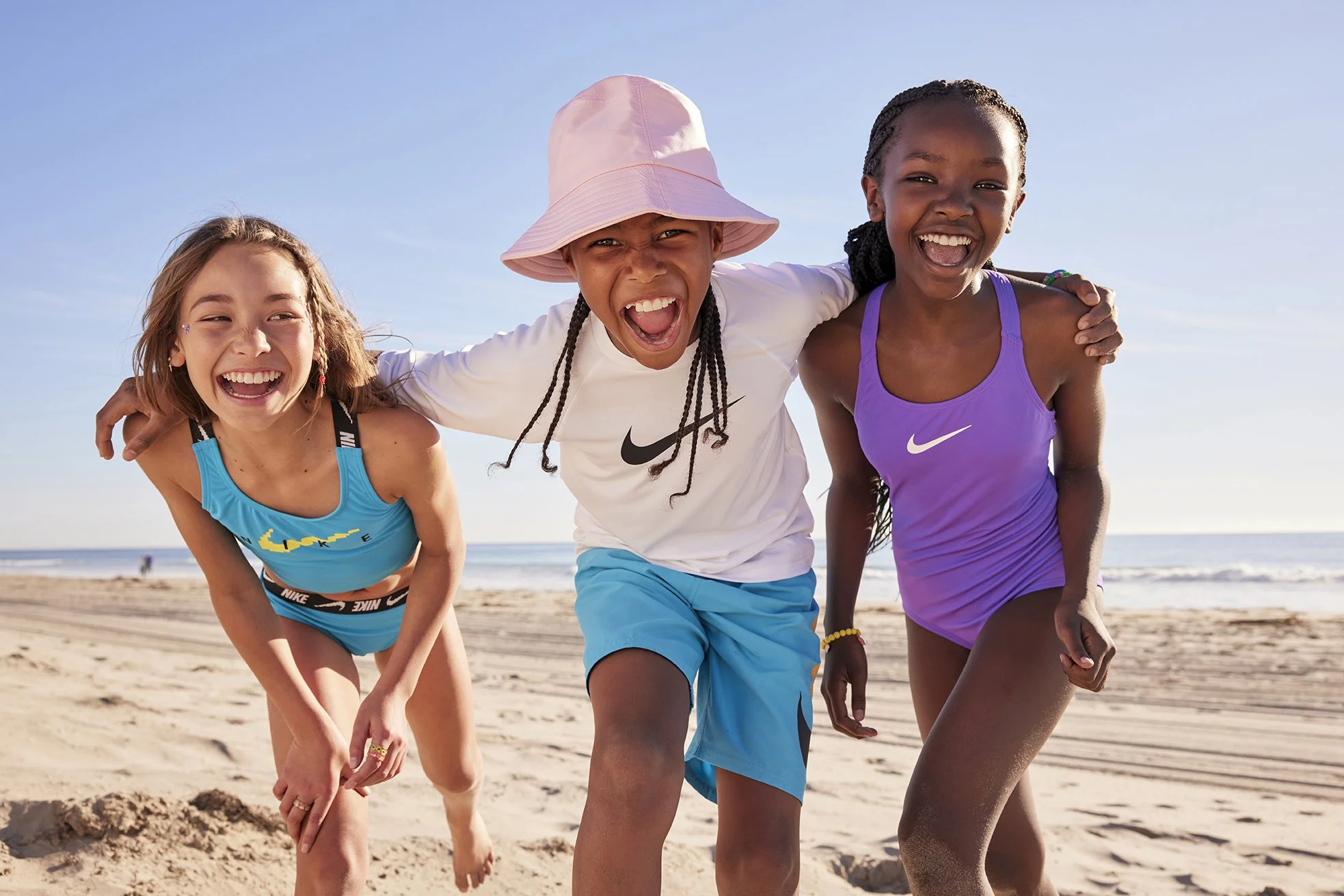 Three young girls playing and smiling on the beach with the ocean in the background.