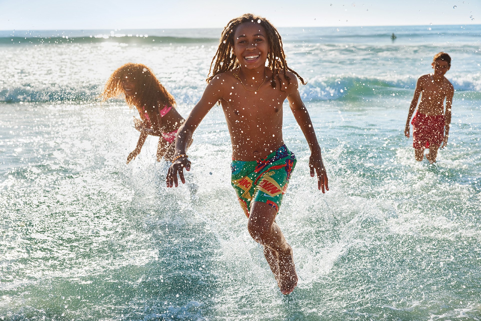 Children playing and running in the shallow ocean water at the beach, smiling and having fun on a sunny day.