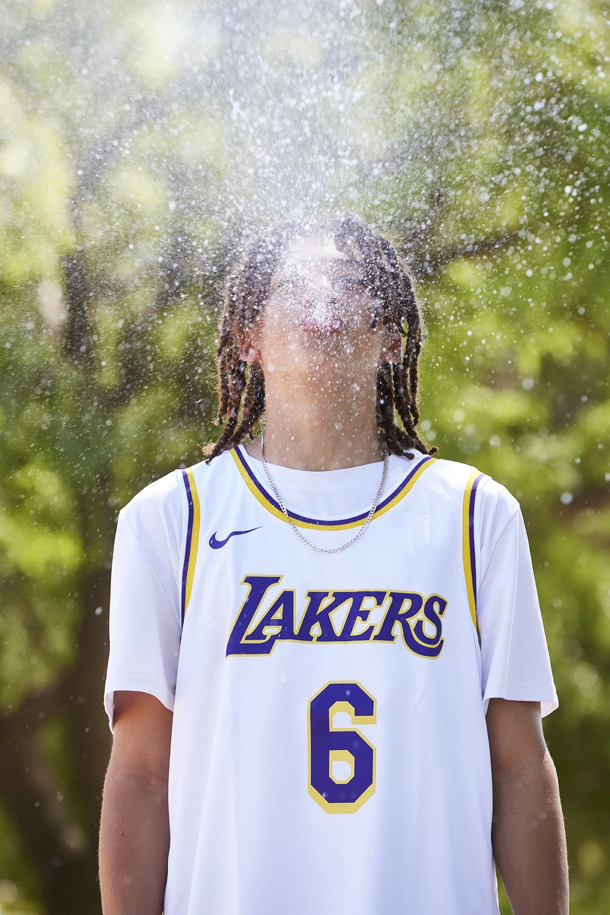 Person in a Lakers basketball jersey with number 6, standing outdoors with water splashing on their face.