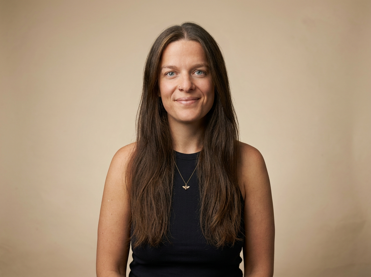 Emily Quested-Lawson, a woman with long brown hair and blue eyes, wearing a black sleeveless top, smiling softly against a neutral beige background.