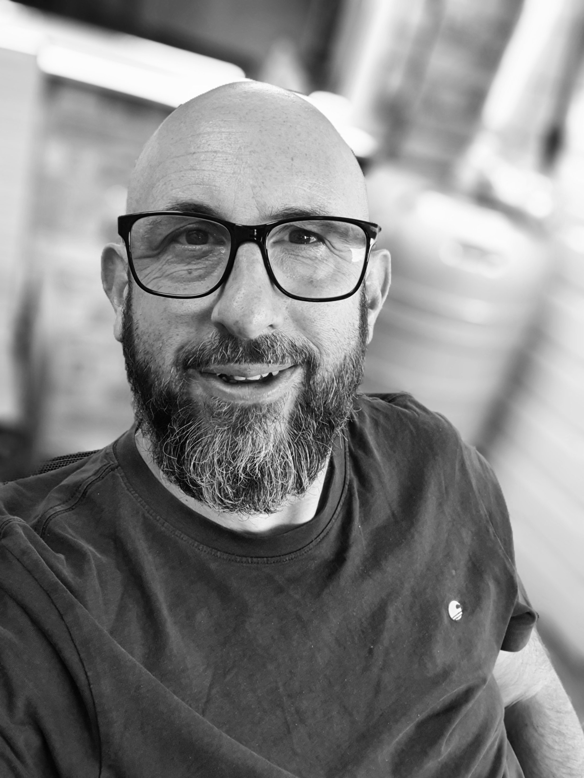 A man with a beard and glasses smiling in a black and white photo.