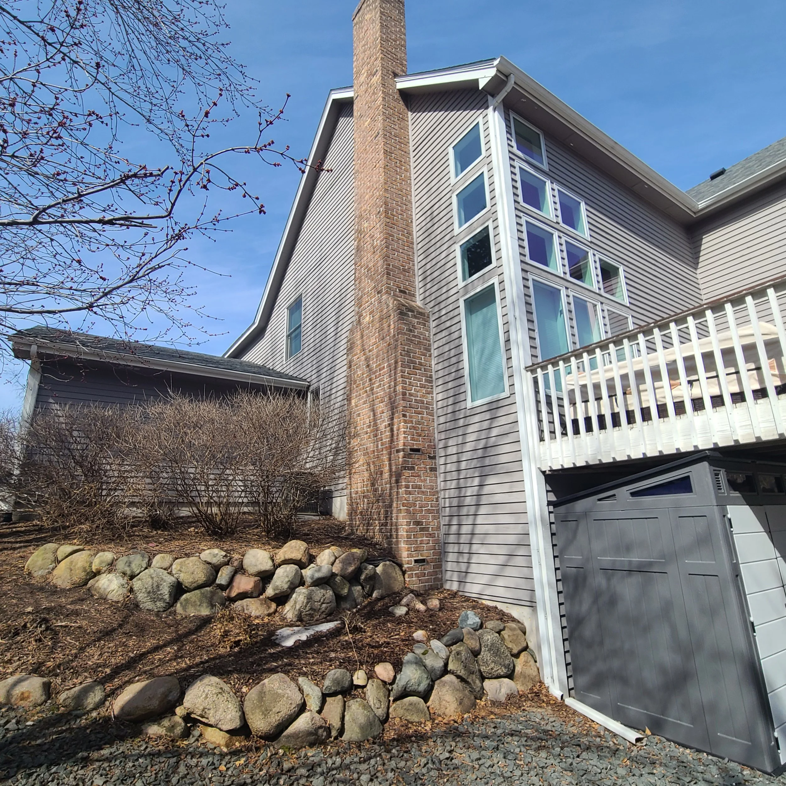 Gray exterior repaint on a Bloomington home with tall window wall and brick chimney detail