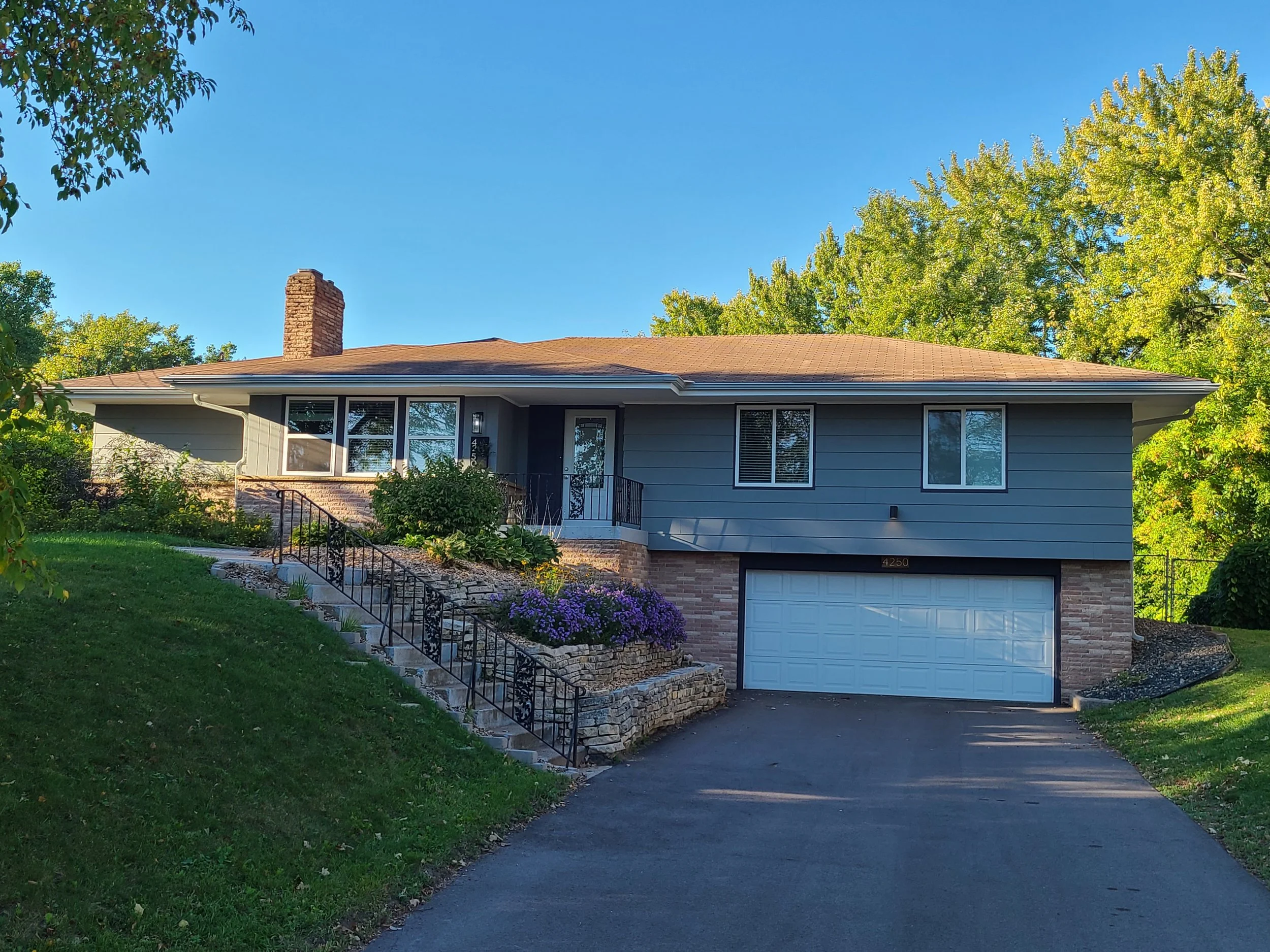 Split-level exterior house painting project in Bloomington, MN featuring gray siding with brick accents on a raised ranch home